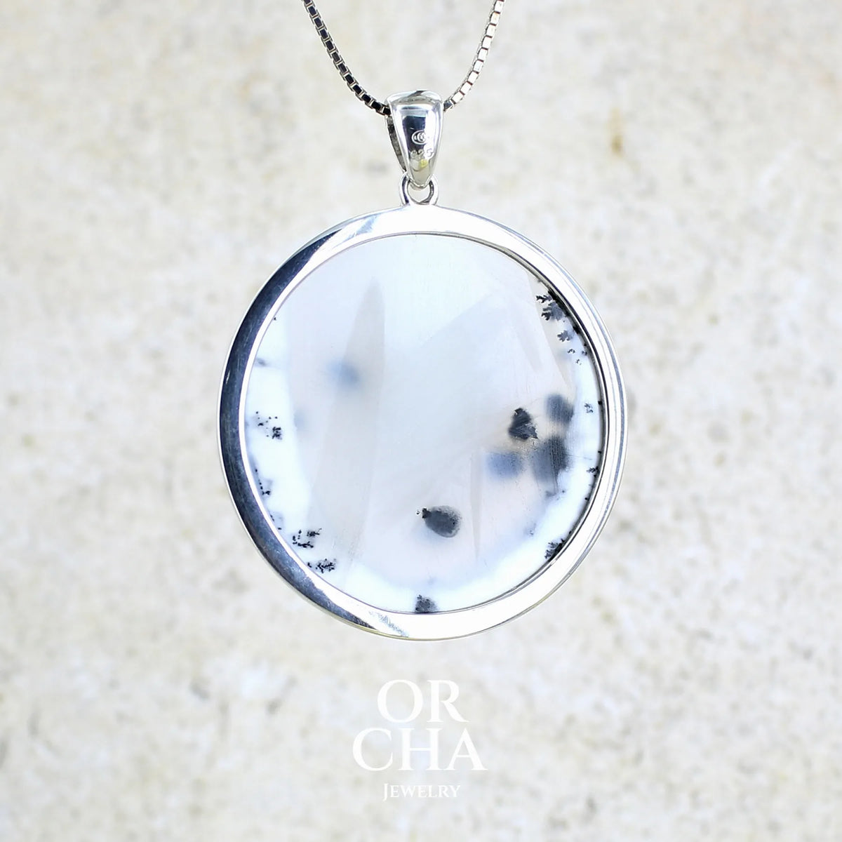 Vue de dos d'un pendentif pour femme en argent massif sertie d'un cabochon rond d'agate dendritique de couleur blanc pur et noir. Pierre opaque à translucide à inclusions paysages de dendrites de manganèse noires contrastées. Bijou unique réalisé par Orchajewelry