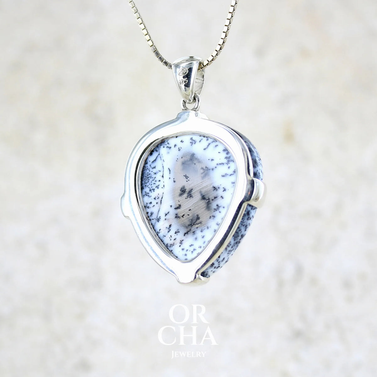 Vue de dos d'un pendentif pour femme en argent massif sertie d'un cabochon en forme de goutte inversée d'agate dendritique de couleur blanc pur et noir. Pierre opaque à translucide à inclusions paysages de dendrites de manganèse noires contrastées. Bijou unique réalisée par Orchajewelry