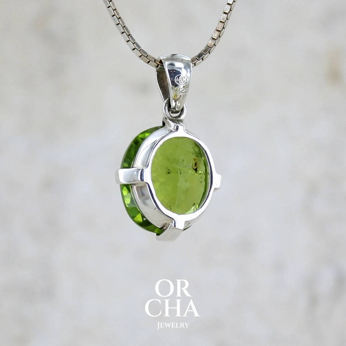 Vue de dos d'un pendentif pour femme en argent massif serti d'un péridot de couleur vert olive doré intense. Pierre taillée, de forme ovale, transparente présentant de nombreuse inclusions. Bijou unique réalisé par Orchajewelry
