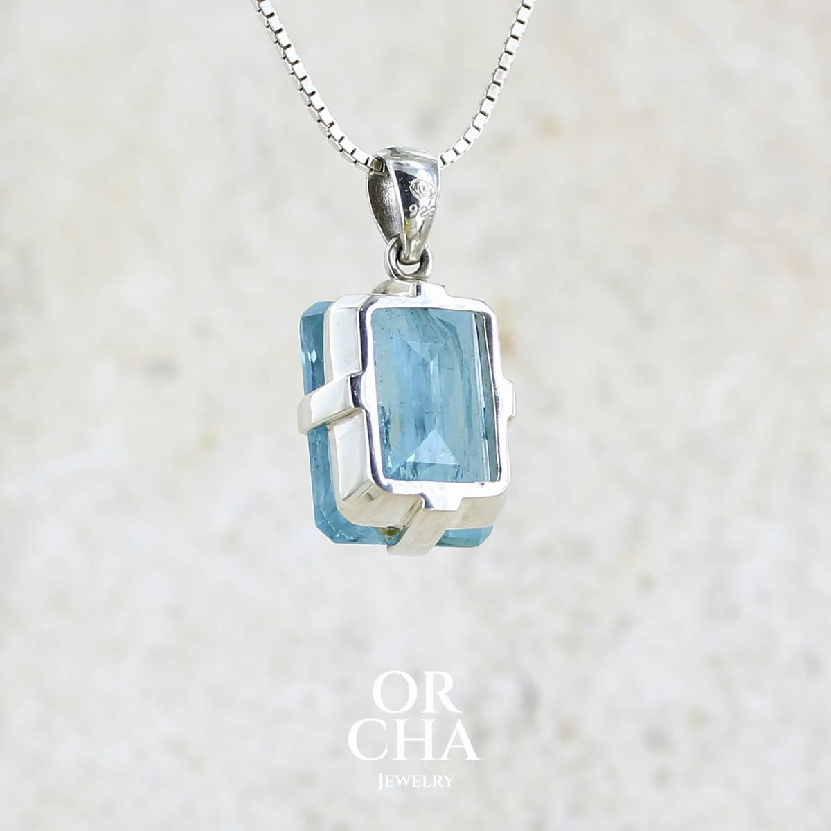Vue de dos d'un pendentif unisexe en argent massif sertie d'une aigue marine taillée de 17 carats de couleur bleu foncé profond et intense, pierre transparente avec de grosses inclusions. Pierre naturelle facettée de forme rectangulaire. Bijoux unique réalisée par Orchajewelry