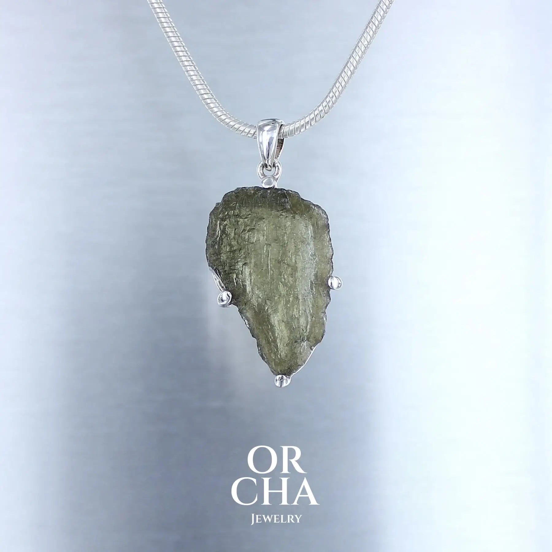 pendentif pour homme en argent massif serti d'une Moldavite brute. Pierre brute naturelle transparente de couleur verte. Bijoux unique, éthique et durable présenté dans un coffret de notre marque, prêt à offrir. Livraison offerte, certificat d'authenticité, service client.