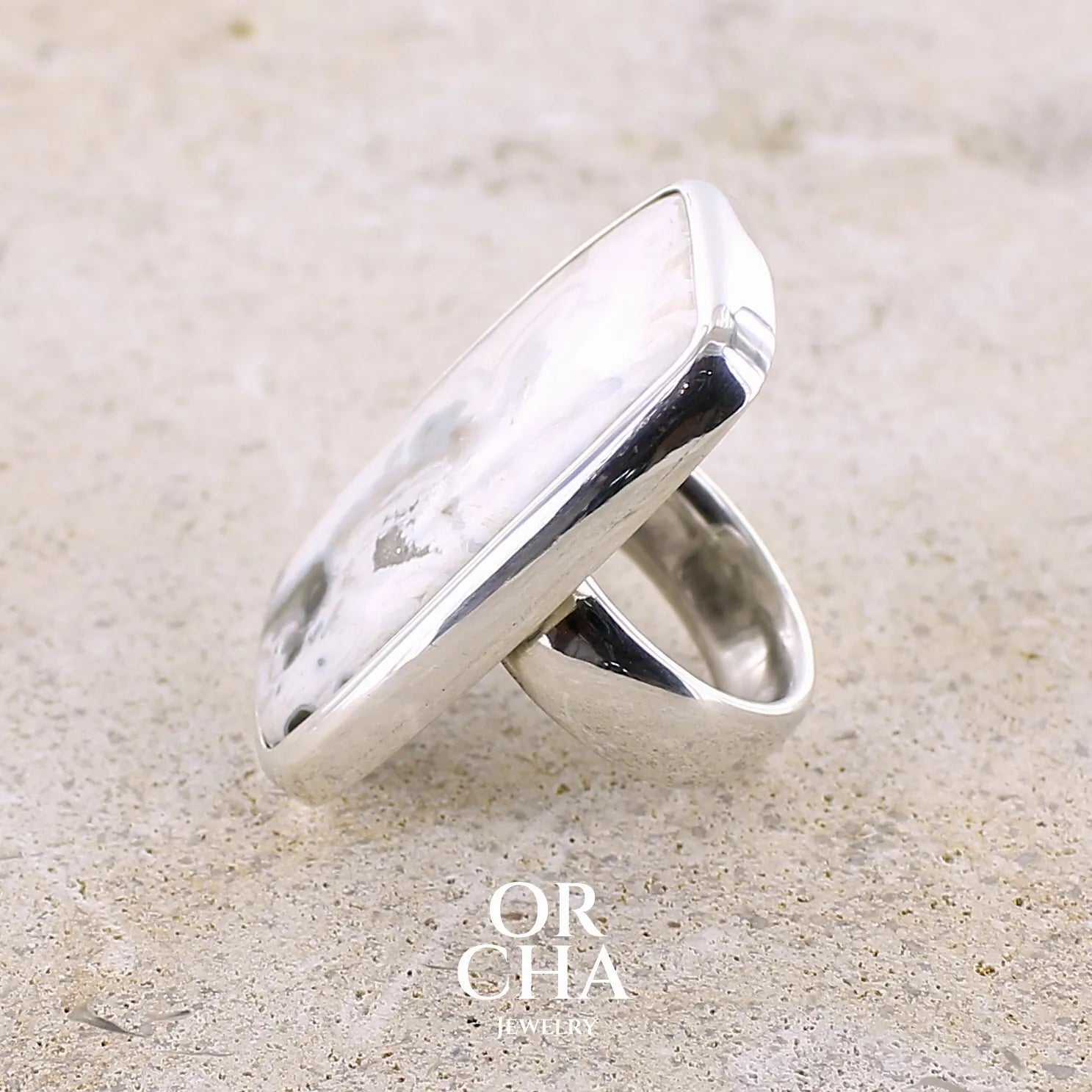 Profil gauche d'une bague pour femme en argent massif sertie d'un cabochon rectangulaire de jaspe océan de couleur blanc crème, gris, kaki et beige. Pierre de qualité opaque. Bijou unique réalisée en taille 54 par Orchajewelry