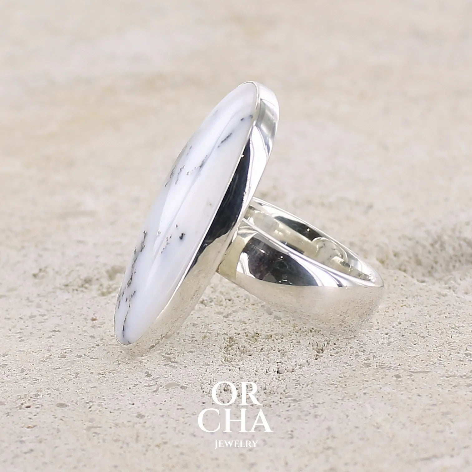 Profil d'une bague pour femme en argent massif sertie d'un cabochon d'agate dendritique de couleur blanche et noire. Pierre de forme ovale de qualité translucide à inclusions paysages de manganèse contrastées. Bijou unique réalisée en taille 58,5 par Orcha Jewelry