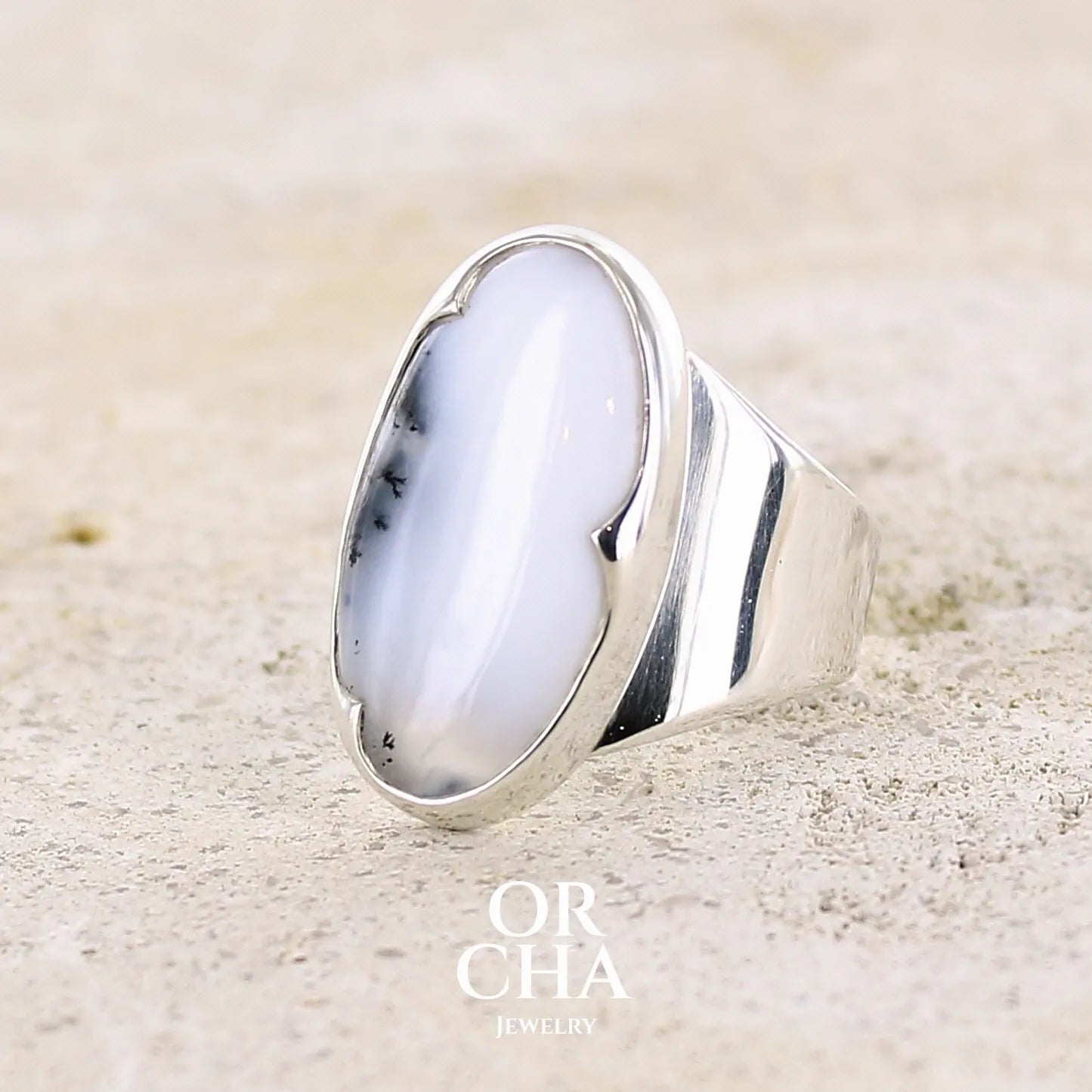 Profil gauche d'une bague pour femme en argent massif sertie d'un cabochon d'agate dendritique de couleur blanche et noire. Pierre de forme ovale de qualité translucide à inclusions paysages de manganèse contrastées. Bijou unique réalisée en taille 58 par Orcha Jewelry