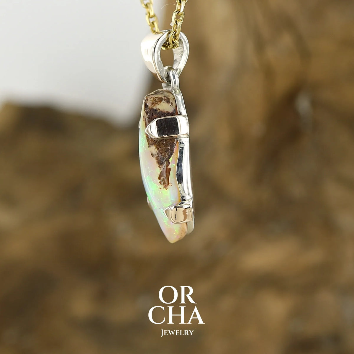 profil d'un pendentif pour femme en or 9k et argent massif 925 serti d'une opale cristal aux feux étoilés multicolores à dominantes vert et jaune. Cabochon de 3,3 carats de forme libre et de qualité translucide avec présence de roche mère. Bijou unique réalisé par Orchajewelry