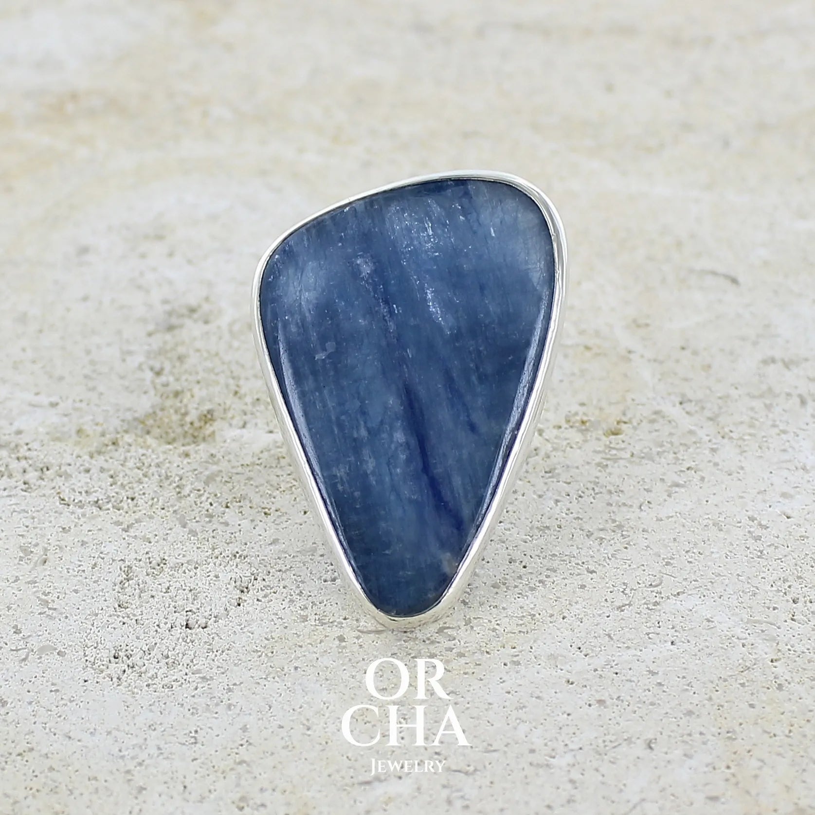 Bague longue et imposante pour femme en argent massif, sertie d'un cabochon de cyanite de couleur bleu jean nacré. Pierre taillée en forme de triangle de qualité translucide. Bijou unique réalisée en taille 58 par Orchajewelry