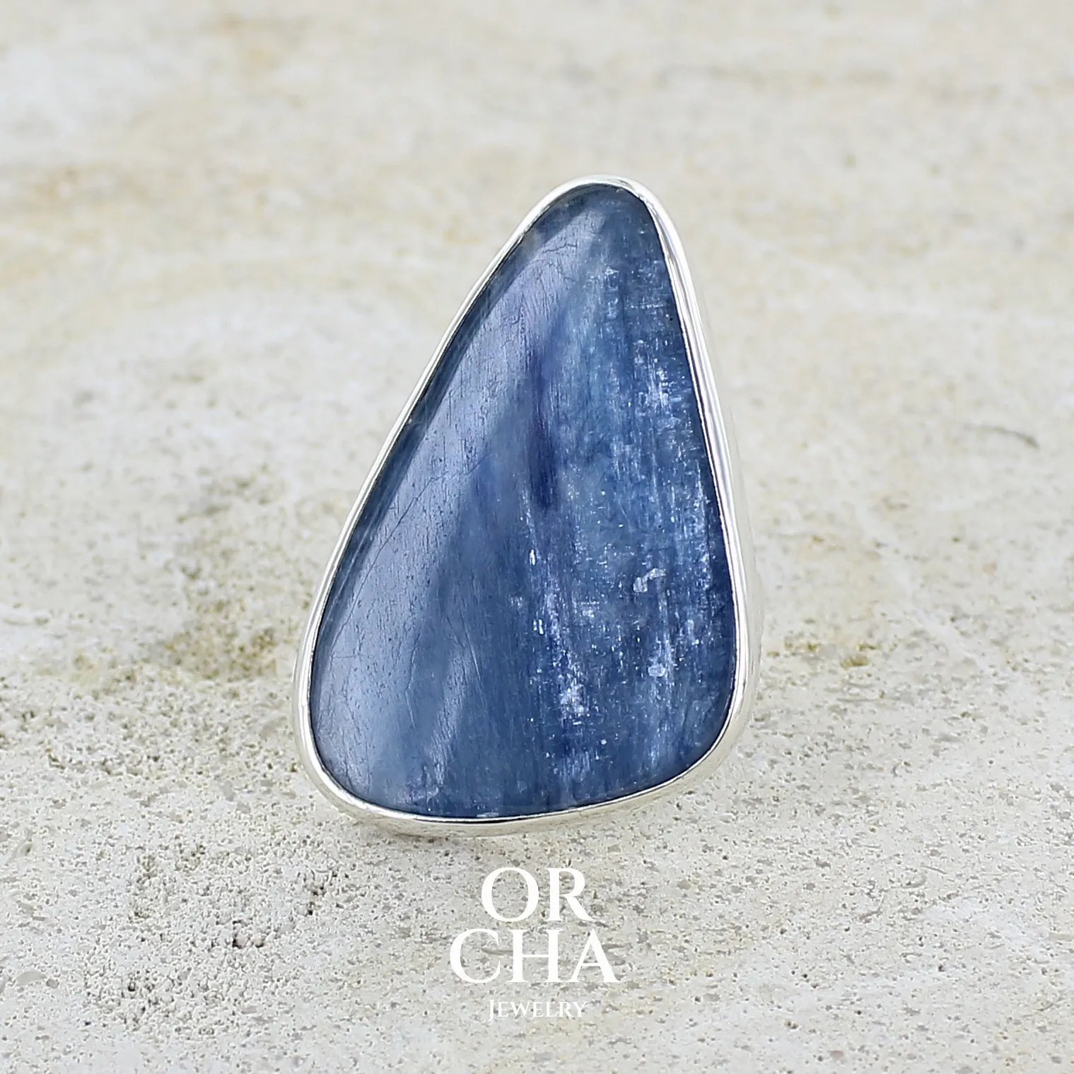 Bague longue et imposante pour femme en argent massif, sertie d'un cabochon de cyanite de couleur bleu jean nacré. Pierre taillée en forme de triangle de qualité translucide. Bijou unique réalisée en taille 58 par Orchajewelry