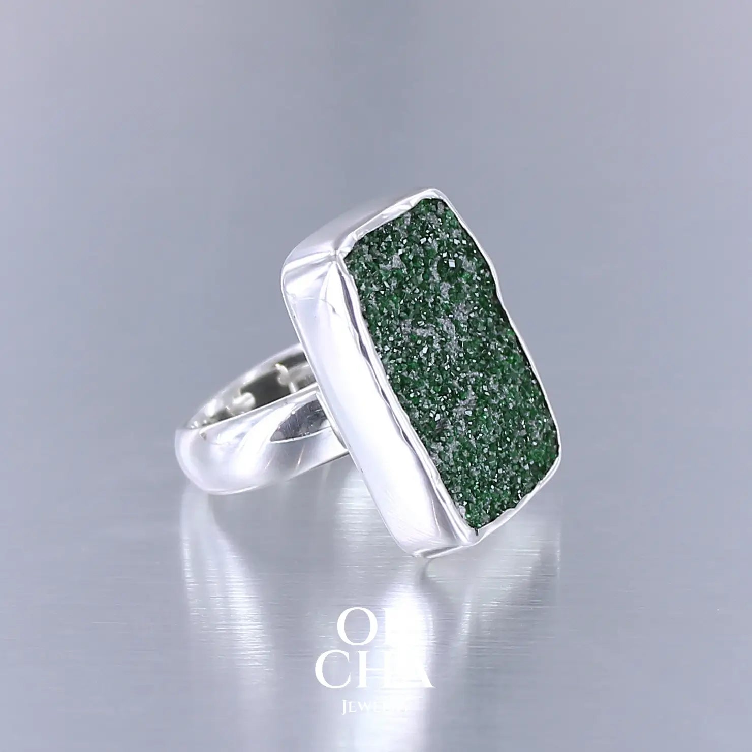 Bague en argent massif sertie d'un grenat Uvarovite brute. Pierre naturelle recouverte de cristaux scintillants de couleur verte. Bague réalisée en taille 55. Bijoux unique, éthique et durable présenté dans un coffret de notre marque, prêt à offrir. Livraison offerte, certificat d'authenticité, service client.