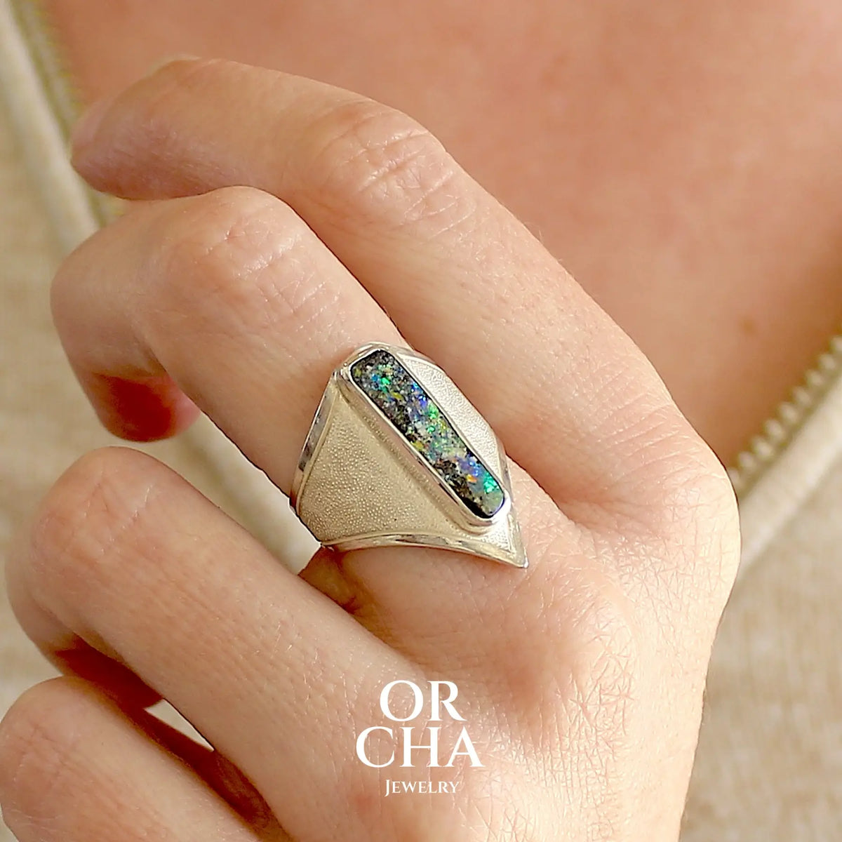 Bague pour femme en argent massif 925 sertie d'une opale boulder aux feux multicolores. Cabochon d'opale massive naturelle taillée en forme de rectangle.. Pierre de qualité opaque. Bague unique réalisée en taille 55 par Orcha Jewelry.