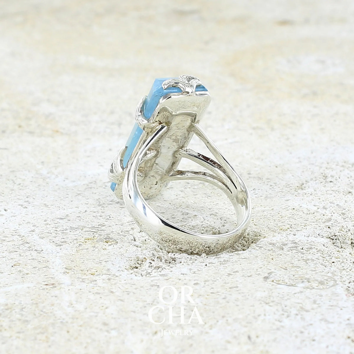 Bague cocktail pour femme en argent massif sertie d'une aigue marine taillée de 15 carats de couleur bleue gris trouble, pierre transparente avec inclusions. Pierre naturelle facettée de forme rectangulaire. Bijoux unique réalisée en taille 54,5 par Orchajewelry