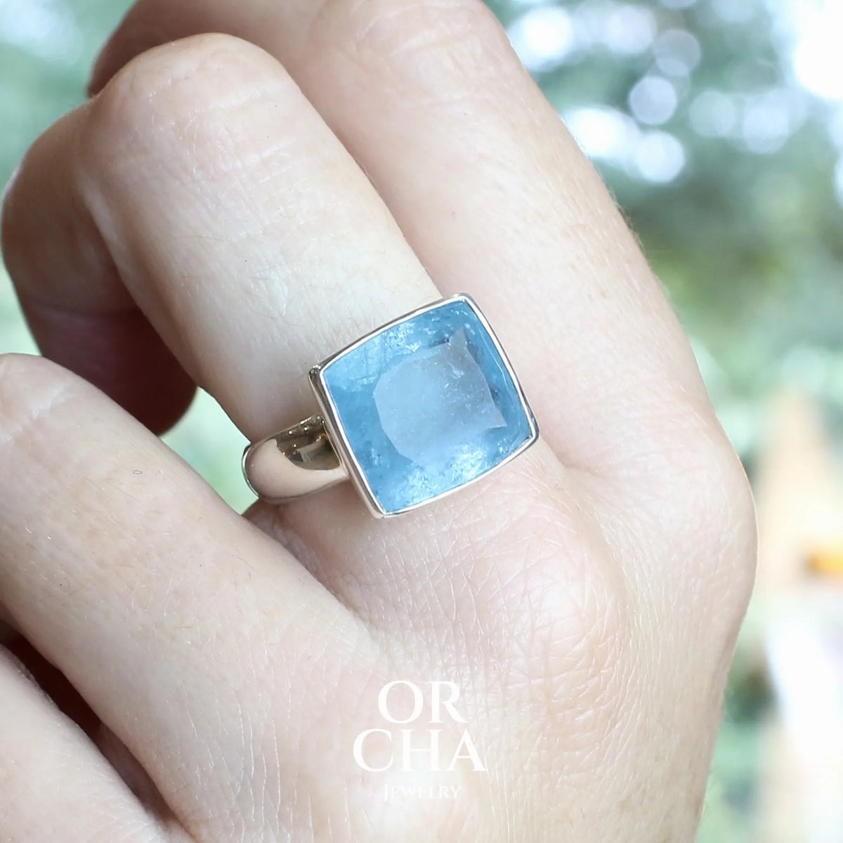 Bague cocktail pour femme en argent massif sertie d'une aigue marine taillée de 10 carats de couleur bleue gris foncé, pierre transparente avec inclusions. Pierre naturelle facettée de forme rectangulaire. Bijoux unique réalisée en taille 60,5 par Orchajewelry