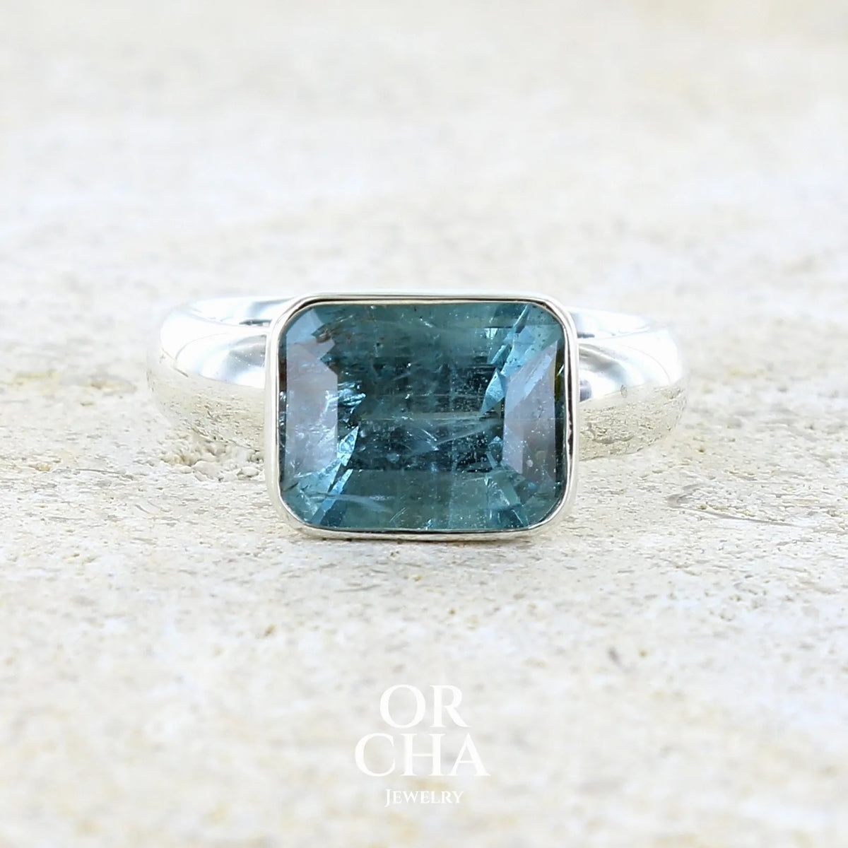 Bague pour femme en argent massif sertie d'une aigue marine taillée de 4 carats de couleur bleue foncé profonde intense et lumineuse, pierre transparente avec inclusions. Pierre naturelle facettée de forme rectangulaire. Bijoux unique réalisée en taille 56 par Orchajewelry