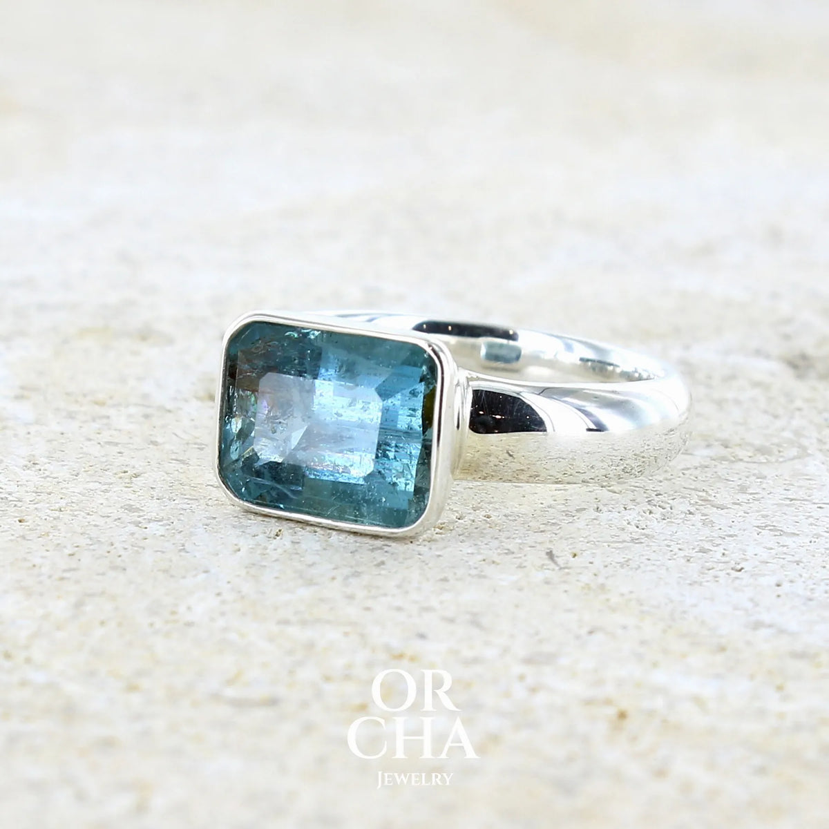 Bague pour femme en argent massif sertie d'une aigue marine taillée de 4 carats de couleur bleue foncé profonde intense et lumineuse, pierre transparente avec inclusions. Pierre naturelle facettée de forme rectangulaire. Bijoux unique réalisée en taille 56 par Orchajewelry
