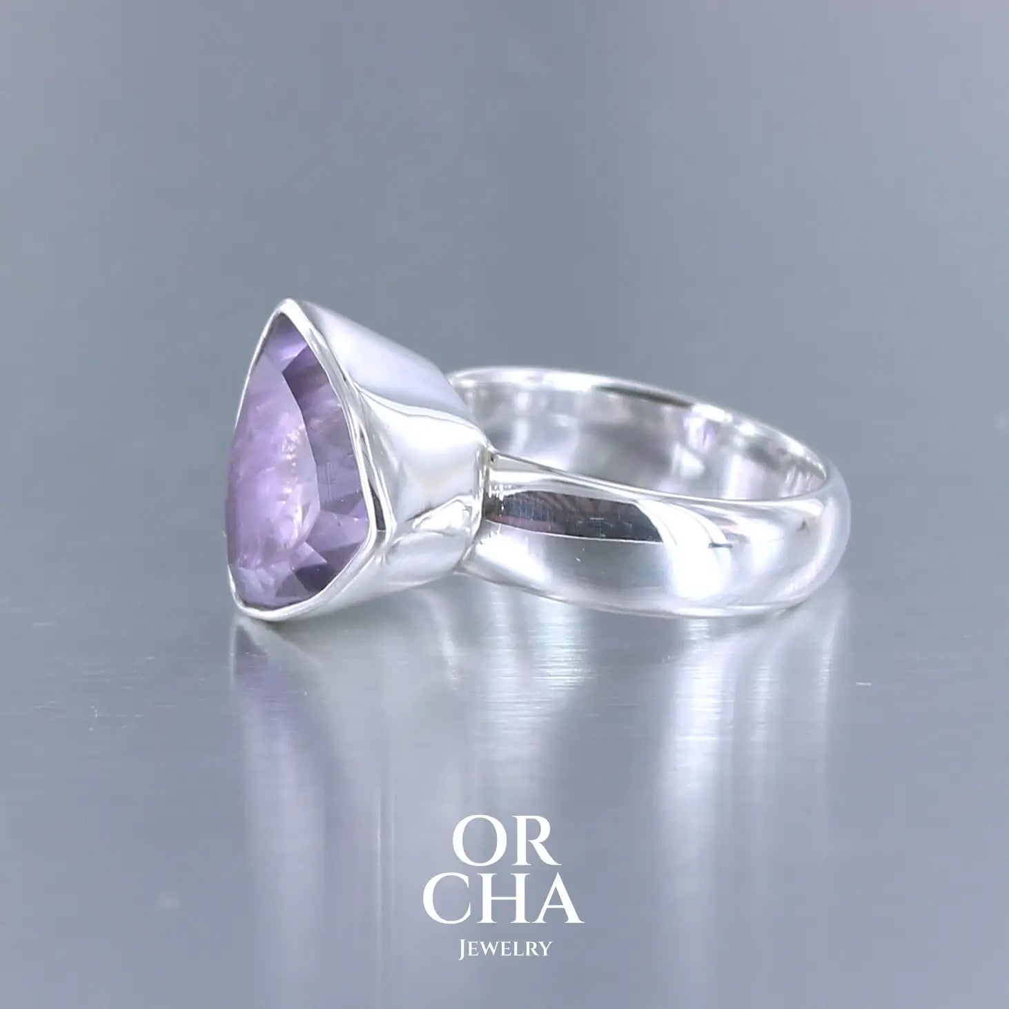 Bague cocktail pour femme en argent massif sertie d'une Améthyste. Pierre taillée trillion de qualité transparente, propre à l'oeil. Pierre naturelle de couleur violette clair gravée de motifs géométriques de fleur de vie. Tailles 58. Bijoux unique, éthique et durable présenté dans un coffret de notre marque, prêt à offrir. Livraison offerte, certificat d'authenticité, service client.