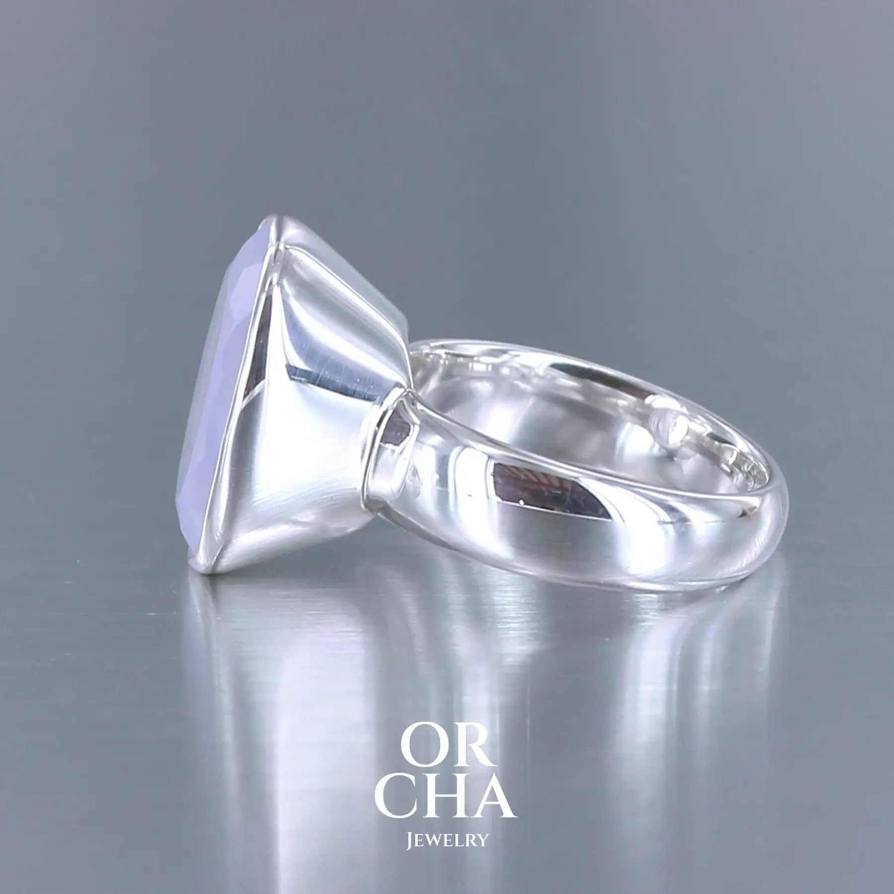Bague cocktail pour femme en argent massif sertie d'un Quartz lavande. Pierre facettée de forme carrée de qualité transparente, propre à l'oeil. Pierre naturelle de couleur violette pastel teintée de rose avec de légers reflets opalescents. Bague réalisée en taille 60. Bijoux unique, éthique et durable présenté dans un coffret de notre marque, prêt à offrir. Livraison offerte, certificat d'authenticité, service client.