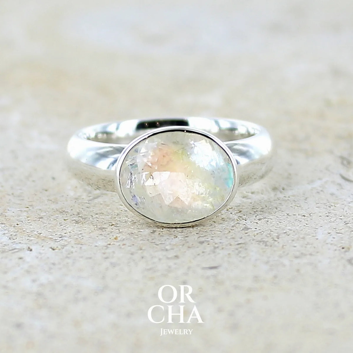 Bague cocktail pour femme en argent massif 925 sertie d'une pierre de lune arc en ciel de Madagascar taillée de 2,5 carats incolore aux reflets bleutés et arc en ciel. Pierre transparente avec inclusions. Bijoux unique réalisée en taille 56 par Orchajewelry