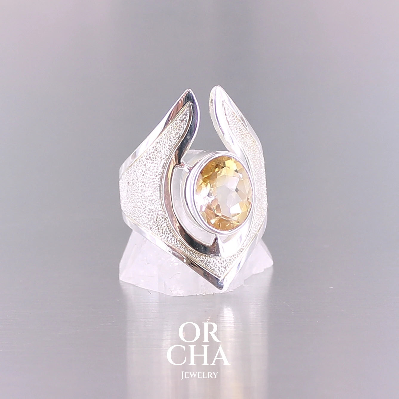 Grande bague contemporaine pour femme en argent massif sertie d'une Citrine. Pierre facettée de forme ovale de qualité transparente, propre à l'oeil. Pierre naturelle de couleur jaune doré lumineux. Bijoux unique, éthique et durable présenté dans un coffret de notre marque, prêt à offrir. Livraison offerte, certificat d'authenticité, service client.