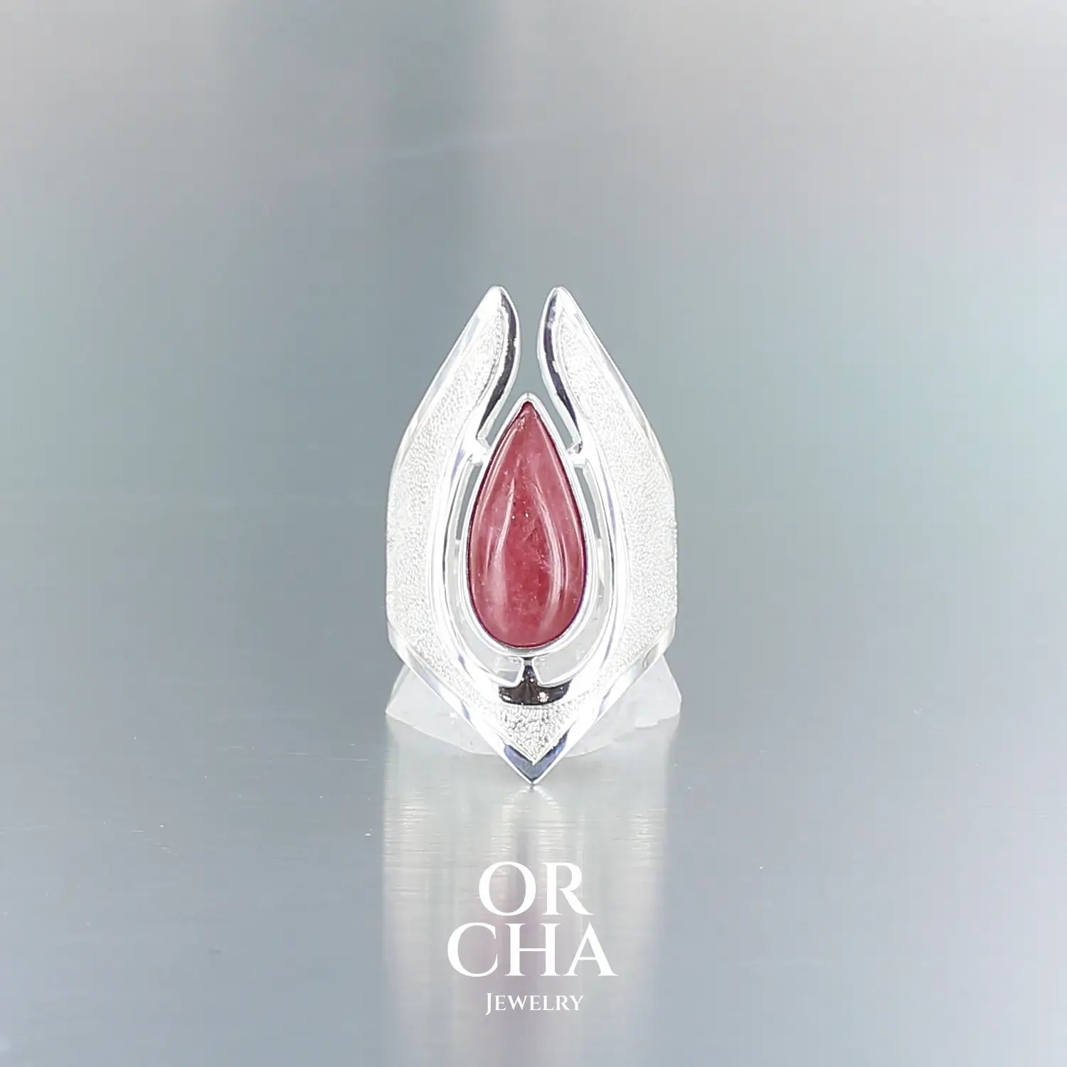 Grande bague pour femme en argent massif sertie d'une Rhodonite. Pierre cabochon en forme de goutte, pierre naturelle de couleur rouge coquelicot. Pierre fine de qualité opaque à translucide présentant des inclusions. Taille 59. Bijoux unique, éthique et durable présenté dans un coffret de notre marque, prêt à offrir. Livraison offerte, certificat d'authenticité, service client.