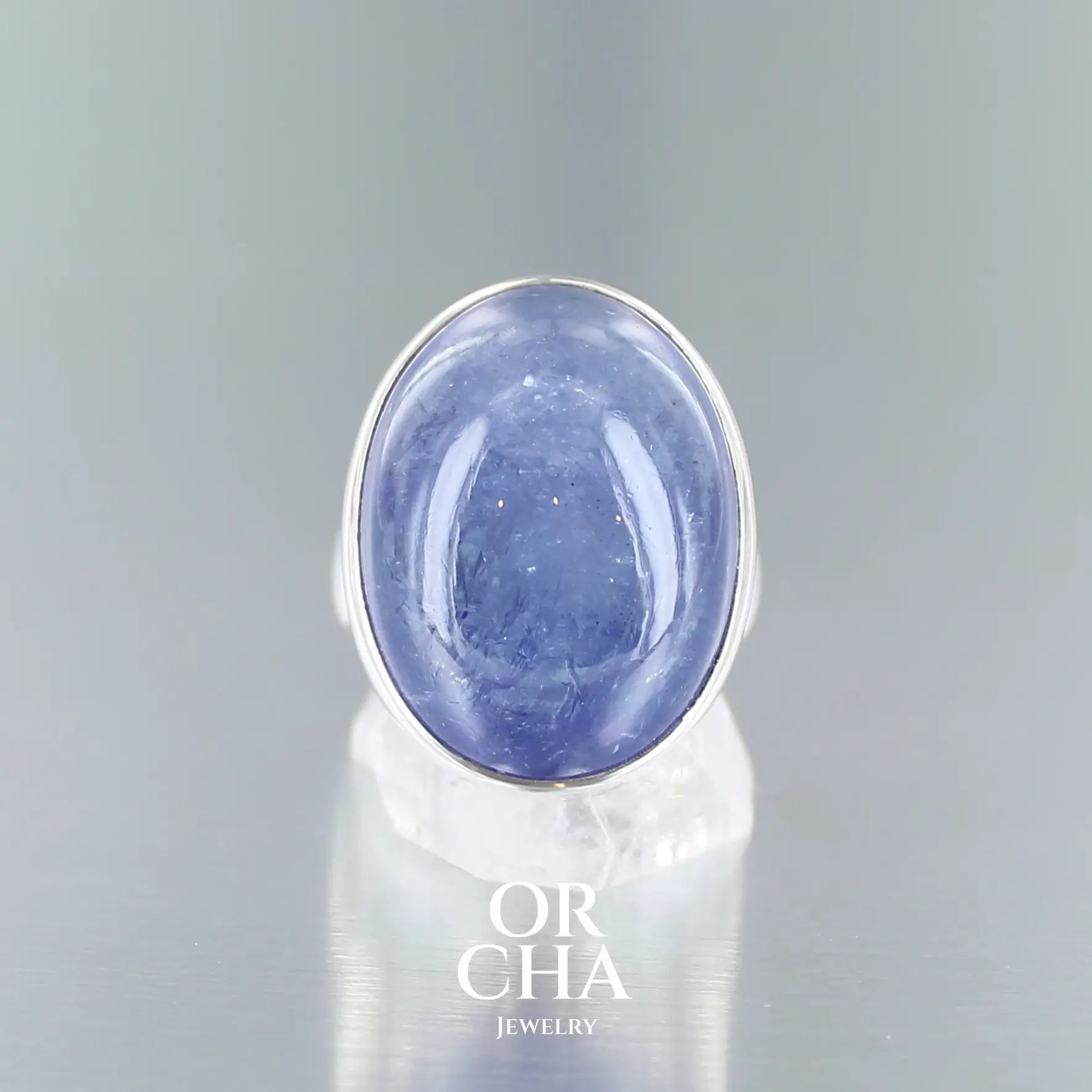 Bague de créateur en argent massif pour femme sertie d'une Tanzanite. Pierre cabochon de forme ovale de qualité translucide avec inclusions. Pierre naturelle de couleur bleu lavande. Bague réalisée en taille 52. Bijoux unique, éthique et durable présenté dans un coffret de notre marque, prêt à offrir. Livraison offerte, certificat d'authenticité, service client.