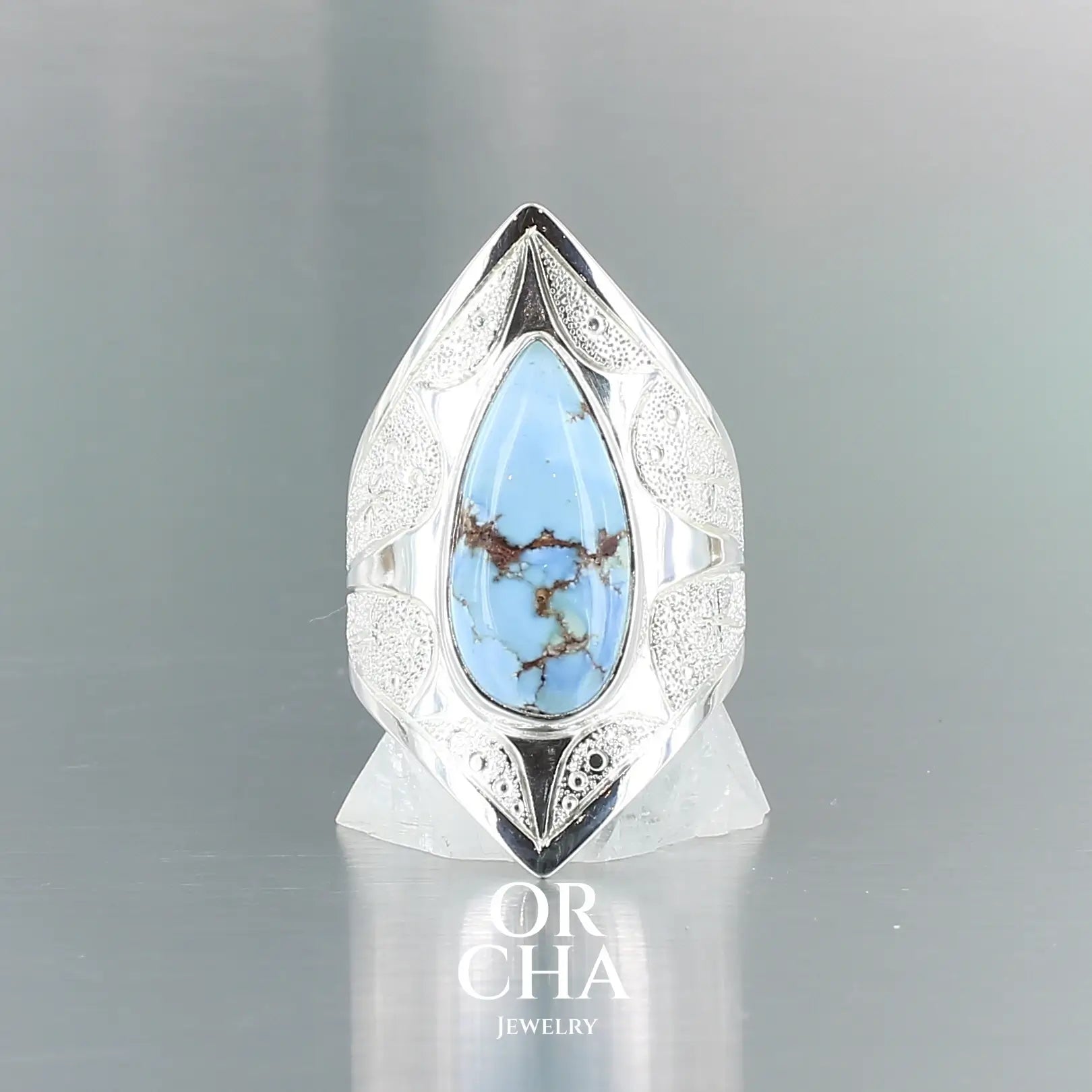 Bague pour femme en argent massif sculptées d'étoiles et autres corps célestes sertie d'une Turquoise Golden Hill. Pierre cabochon en forme de goutte, pierre naturelle aux nuances de bleus . Qualité opaque, pierre non stabilisée. Taille 54. Bijoux unique, éthique et durable présenté dans un coffret de notre marque, prêt à offrir. Livraison offerte, certificat d'authenticité, service client.