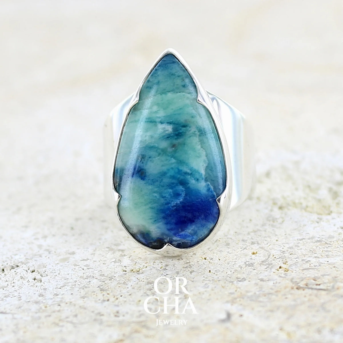 Bague pour femme en argent massif sertie d'un cabochon d'afghane de couleur bleu et bleu gris vert. Pierre taillée en forme de goutte de qualité opaque à inclusions (petites fissures) en surface, fréquente et admise sur ce type de pierre. Bijou unique réalisée en taille 58 par Orchajewelry