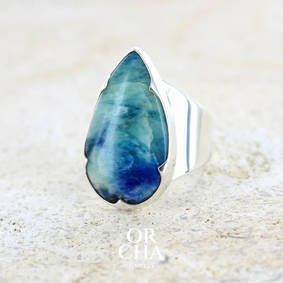 Bague pour femme en argent massif sertie d'un cabochon d'afghane de couleur bleu et bleu gris vert. Pierre taillée en forme de goutte de qualité opaque à inclusions (petites fissures) en surface, fréquentes et admises sur ce type de pierre. Bijou unique réalisée en taille 58 par Orchajewelry