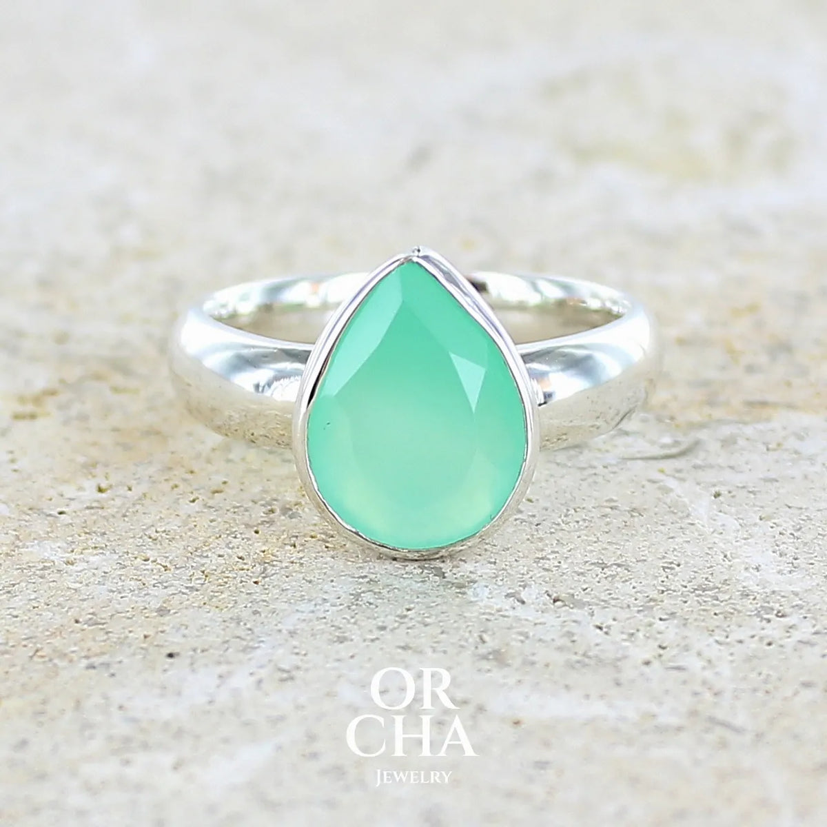 Bague pour femme en argent massif sertie d'un cabochon de chrysoprase de couleur vert émeraude pastel. Pierre translucide taillée en forme de goutte. Bijou unique réalisé en taille 58 par Orcha Jewelry