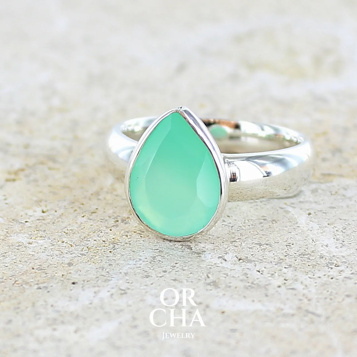 Bague pour femme en argent massif sertie d'un cabochon de chrysoprase de couleur vert émeraude pastel. Pierre translucide taillée en forme de goutte. Bijou unique réalisé en taille 58 par Orcha Jewelry