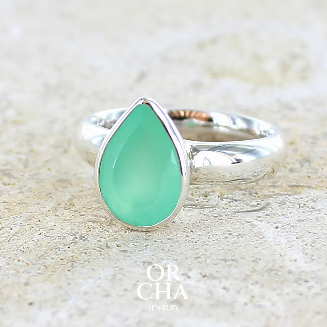 Bague pour femme en argent massif sertie d'un cabochon de chrysoprase de couleur vert émeraude pastel. Pierre translucide taillée en forme de goutte. Bijou unique réalisé en taille 56 par Orcha Jewelry