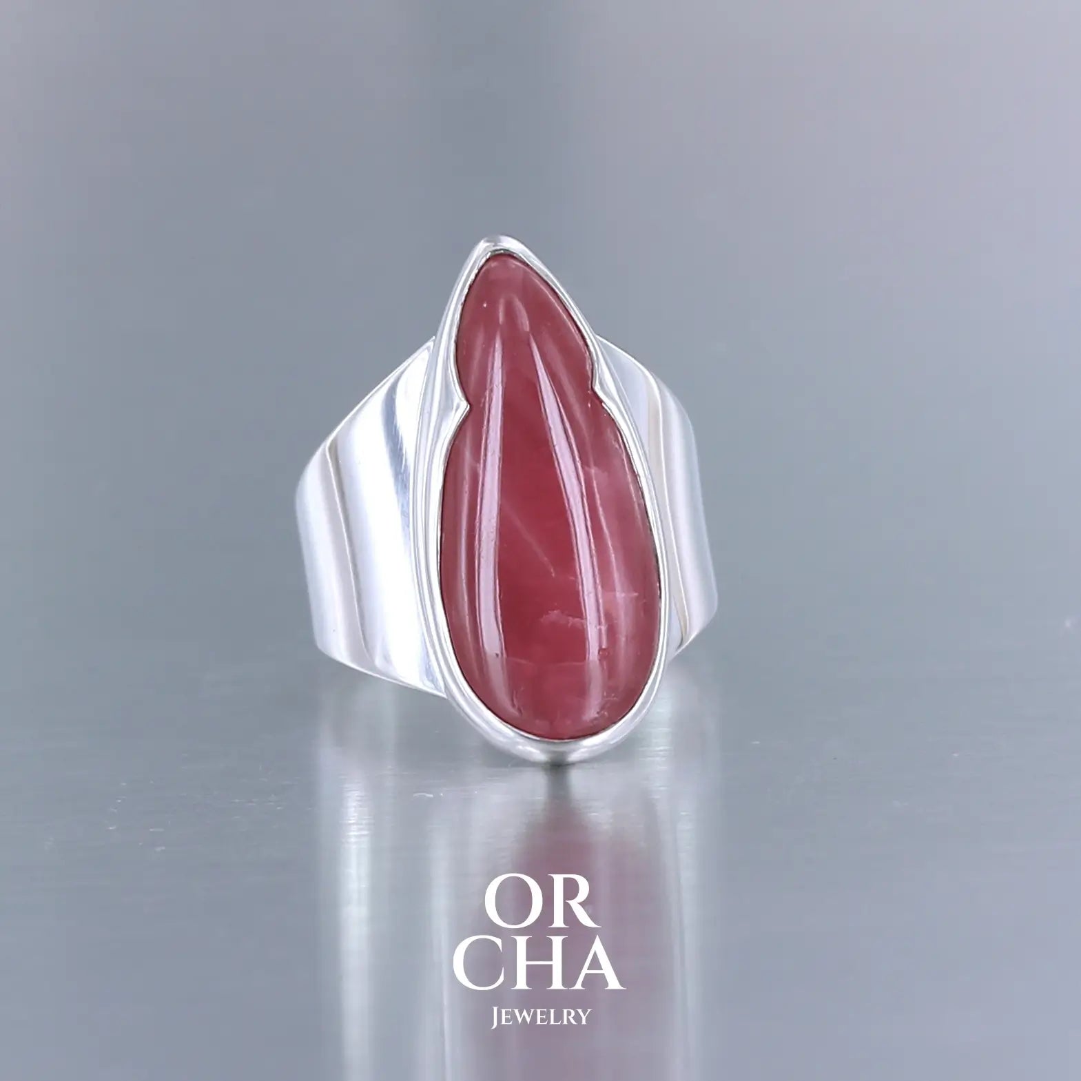 Grande bague pour femme en argent massif sertie d'une Rhodonite. Pierre cabochon en forme de goutte, pierre naturelle de qualité rare de couleur rouge coquelicot. Pierre fine de qualité opaque. Taille 56. Bijoux unique, éthique et durable présenté dans un coffret de notre marque, prêt à offrir. Livraison offerte, certificat d'authenticité, service client.