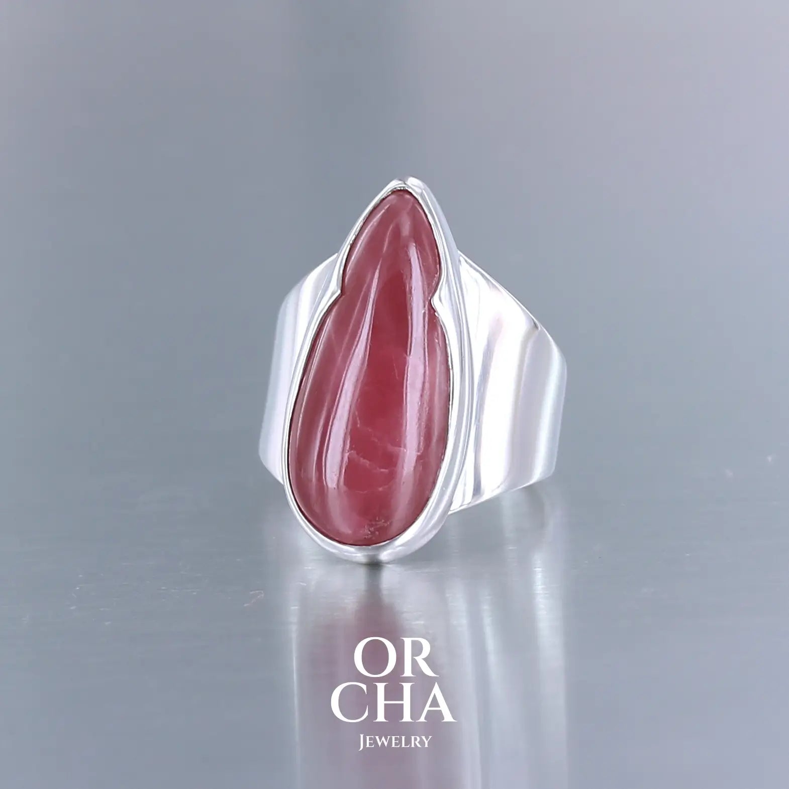 Grande bague pour femme en argent massif sertie d'une Rhodonite. Pierre cabochon en forme de goutte, pierre naturelle de qualité rare de couleur rouge coquelicot. Pierre fine de qualité opaque. Taille 56. Bijoux unique, éthique et durable présenté dans un coffret de notre marque, prêt à offrir. Livraison offerte, certificat d'authenticité, service client.