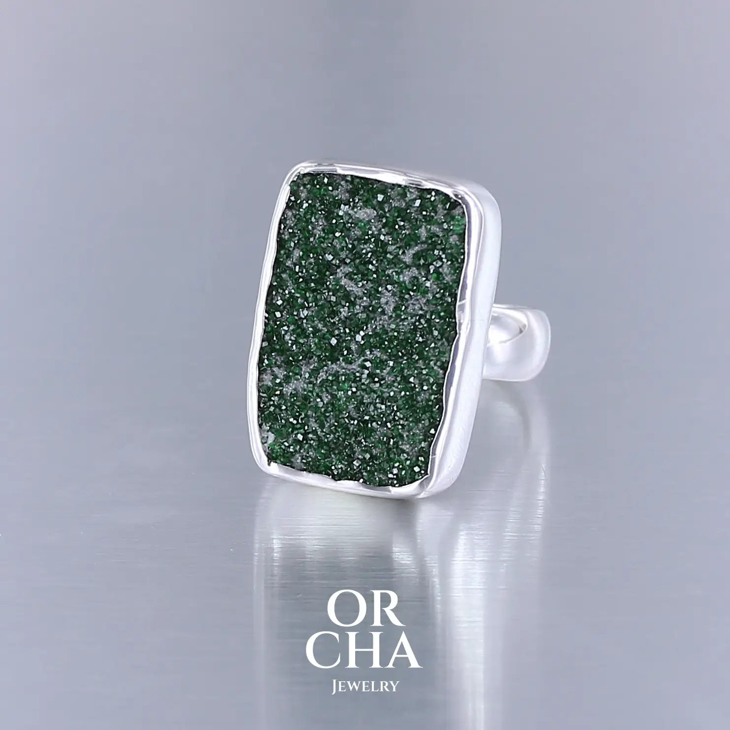 Bague en argent massif sertie d'un grenat Uvarovite brute. Pierre naturelle recouverte de cristaux scintillants de couleur verte. Bague réalisée en taille 55. Bijoux unique, éthique et durable présenté dans un coffret de notre marque, prêt à offrir. Livraison offerte, certificat d'authenticité, service client.