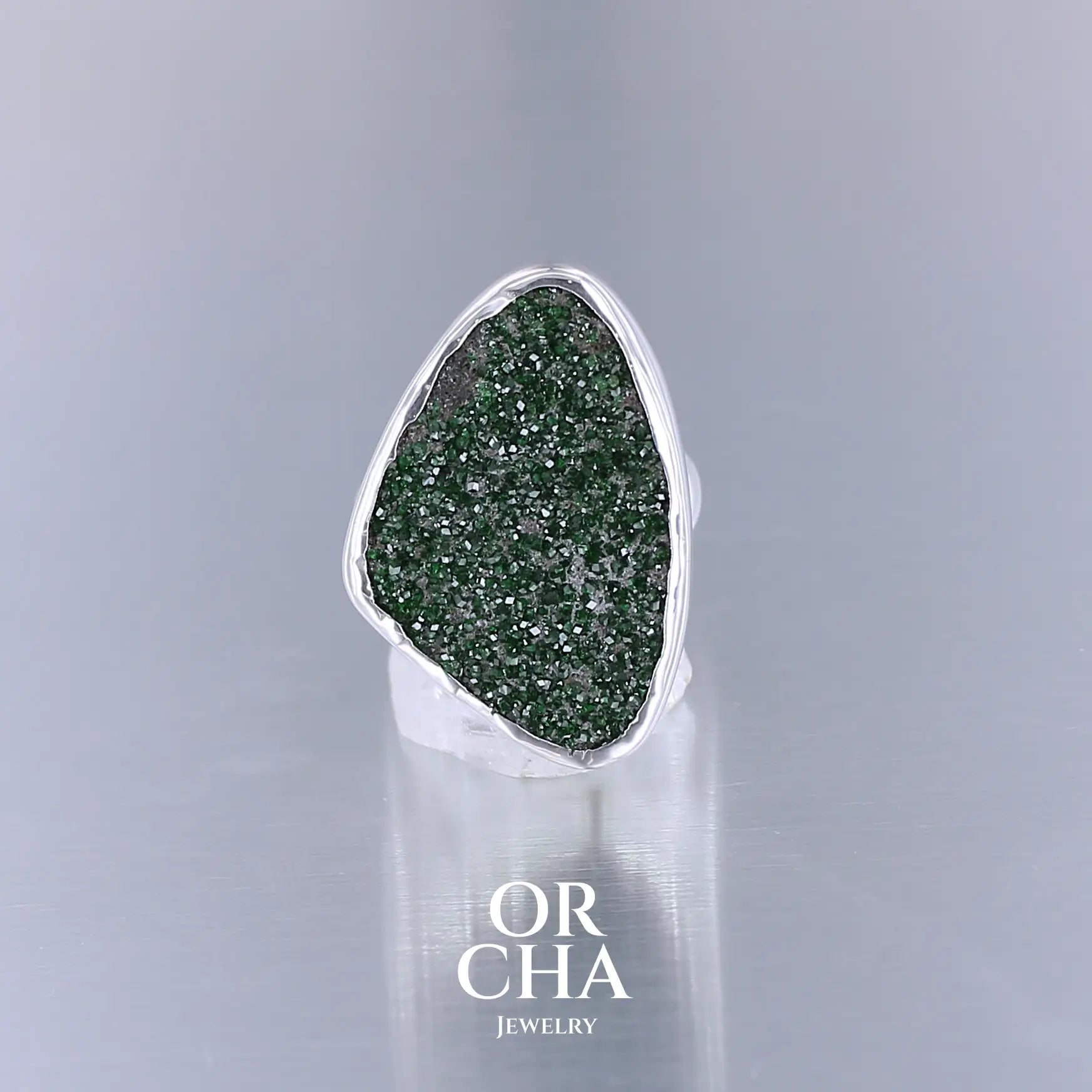 Bague en argent massif serti d'un grenat Uvarovite brute. Pierre naturelle recouverte de cristaux scintillants de couleur verte. Bague réalisée en taille 55. Bijoux unique, éthique et durable présenté dans un coffret de notre marque, prêt à offrir. Livraison offerte, certificat d'authenticité, service client.