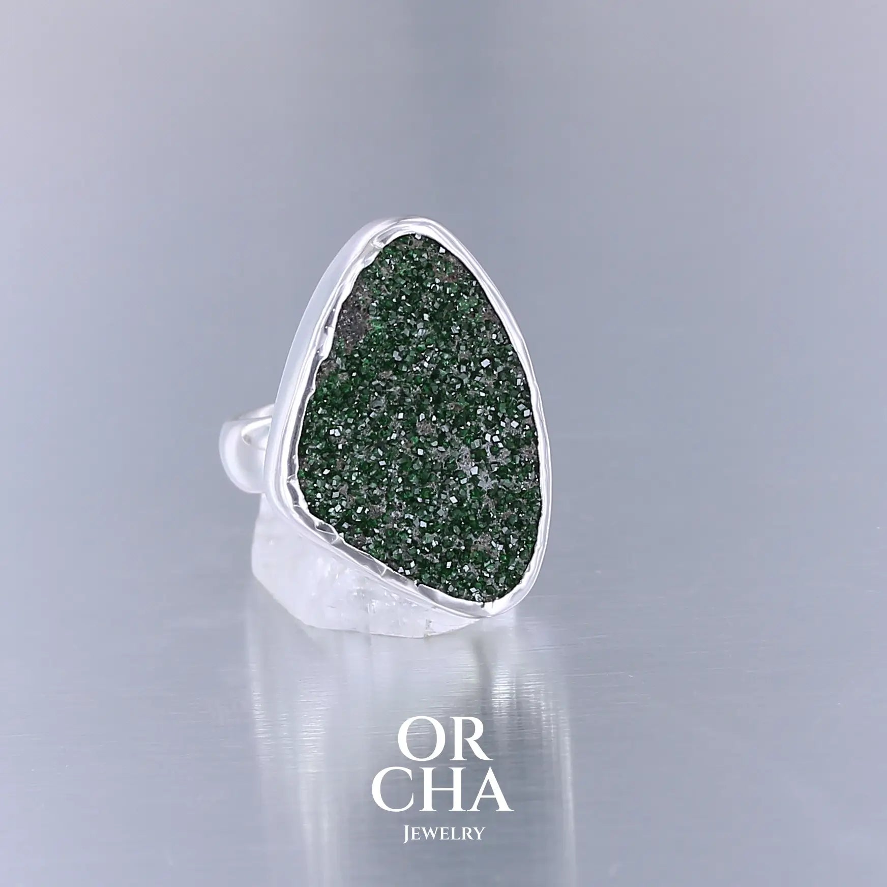 Bague en argent massif serti d'un grenat Uvarovite brute. Pierre naturelle recouverte de cristaux scintillants de couleur verte. Bague réalisée en taille 55. Bijoux unique, éthique et durable présenté dans un coffret de notre marque, prêt à offrir. Livraison offerte, certificat d'authenticité, service client.