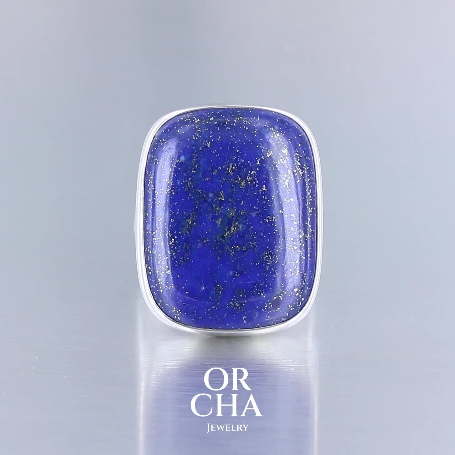 Bague en argent massif ornée d'un lapis lazuli de forme rectangulaire aux angles arrondis. La pierre présente une couleur bleu profond mouchetée de fines inclusions dorées de pyrite. Le sertissage est lisse et épuré, encadrant parfaitement la pierre, mettant en valeur son éclat naturel et sa texture minérale. Un bague élégante et sobre. Bijoux unique, éthique et durable présenté dans un coffret de notre marque, prêt à offrir. Livraison offerte, certificat d'authenticité, service client.