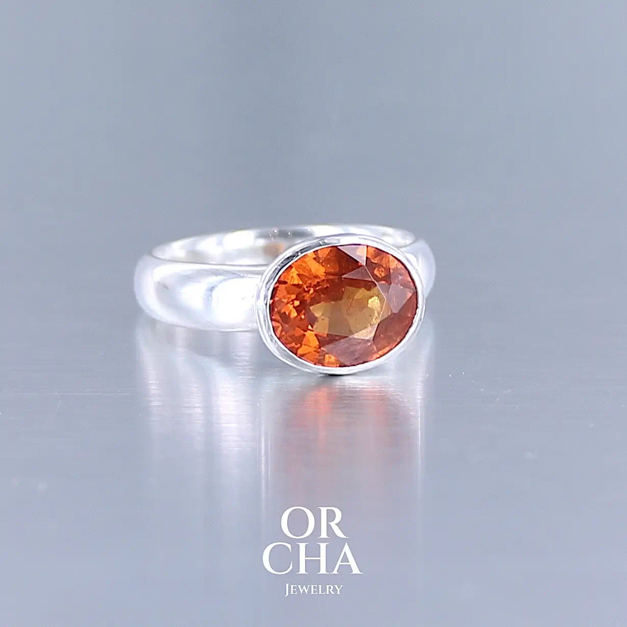 Profil d'une bague cocktail pour femme en argent massif sertie d'un Grenat Spessartite. Pierre facettée de forme ovale de qualité transparente, propre à l'oeil. Pierre naturelle de couleur orange intense, ce Grenat est également appelé Grenat "Fanta" en rapport à la couleur saturé du célèbre soda. Tailles 58.5. Bijoux unique, éthique et durable présenté dans un coffret de notre marque, prêt à offrir. Livraison offerte, certificat d'authenticité, service client.