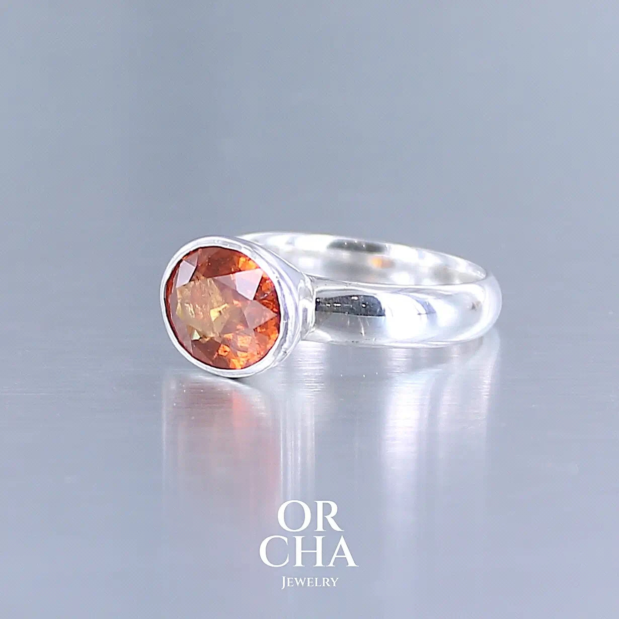 Profil d'une bague cocktail pour femme en argent massif sertie d'un Grenat Spessartite. Pierre facettée de forme ovale de qualité transparente, propre à l'oeil. Pierre naturelle de couleur orange intense, ce Grenat est également appelé Grenat "Fanta" en rapport à la couleur saturé du célèbre soda. Tailles 58.5. Bijoux unique, éthique et durable présenté dans un coffret de notre marque, prêt à offrir. Livraison offerte, certificat d'authenticité, service client.