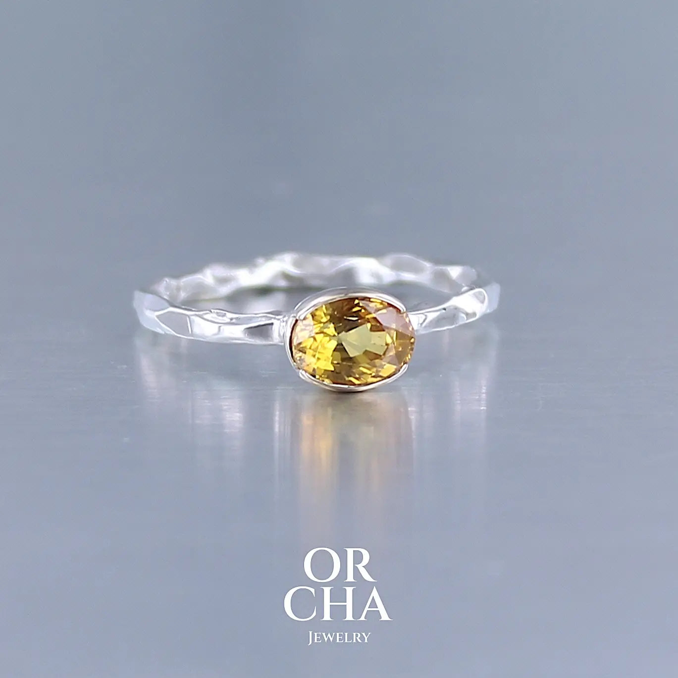 Photo de profil d'une bague anneau pour femme en argent massif et or 12 k sertie d'un Saphir jaune orangé très lumineux. Pierre facettée de forme ovale, de qualité transparente, propre à l'oeil. Pierre chauffée et traitée au beryllium. Bijoux unique, éthique et durable présenté dans un coffret de notre marque, prêt à offrir. Livraison offerte, certificat d'authenticité, service client.