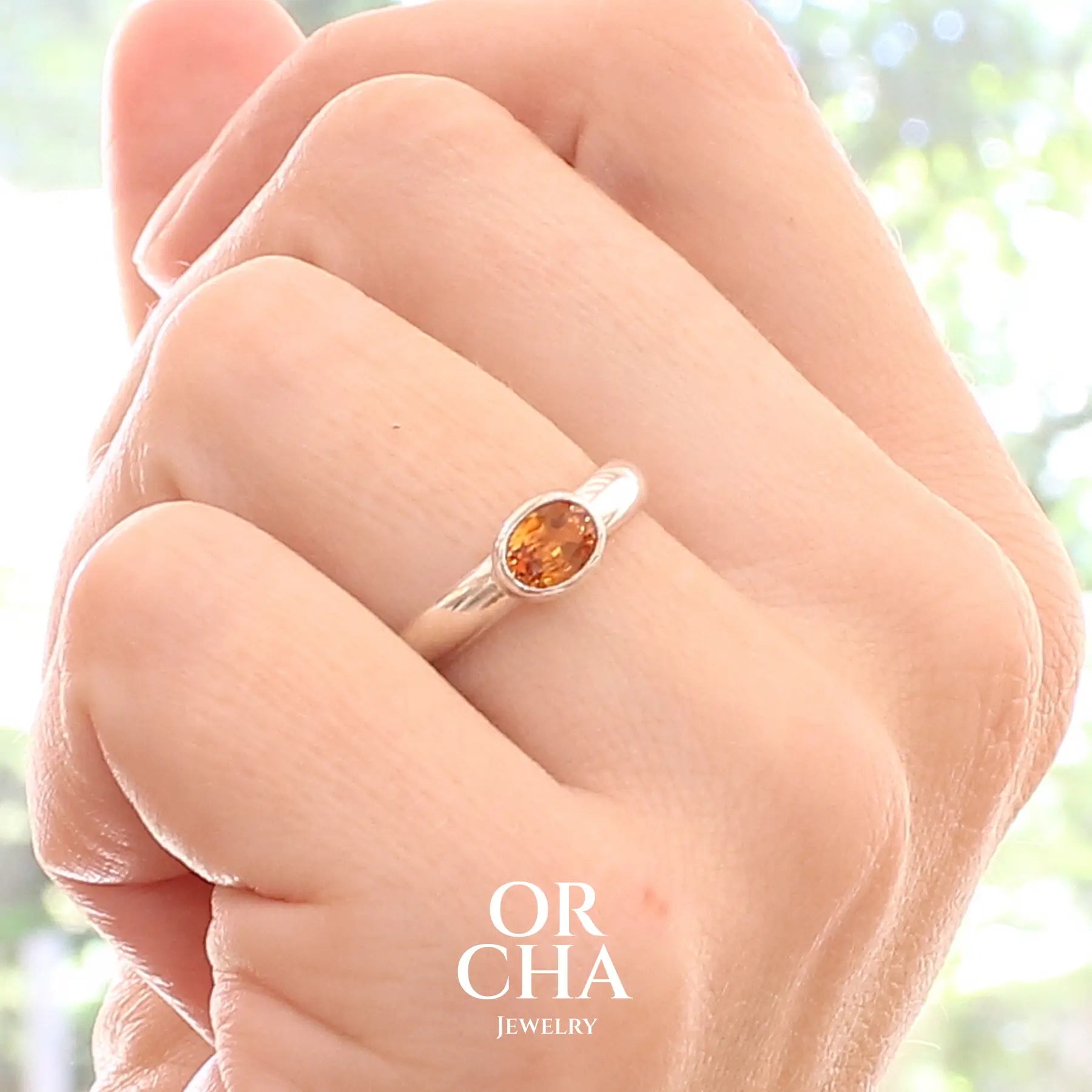 photo sur modèle d'une bague anneau en argent massif sertie d'un Saphir orange. Pierre facettée de forme ovale de qualité transparente, propre à l'oeil. Pierre chauffe et traité au beryllium de couleur orange intense. Tailles 56. Pour homme et femme. Bijoux unique, éthique et durable présenté dans un coffret de notre marque, prêt à offrir. Livraison offerte, certificat d'authenticité, service client.