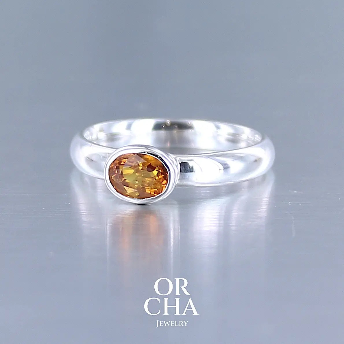 photo de profil d'une bague anneau en argent massif sertie d'un Saphir orange. Pierre facettée de forme ovale de qualité transparente, propre à l'oeil. Pierre chauffe et traité au beryllium de couleur orange intense. Tailles 56. Pour homme et femme. Bijoux unique, éthique et durable présenté dans un coffret de notre marque, prêt à offrir. Livraison offerte, certificat d'authenticité, service client.