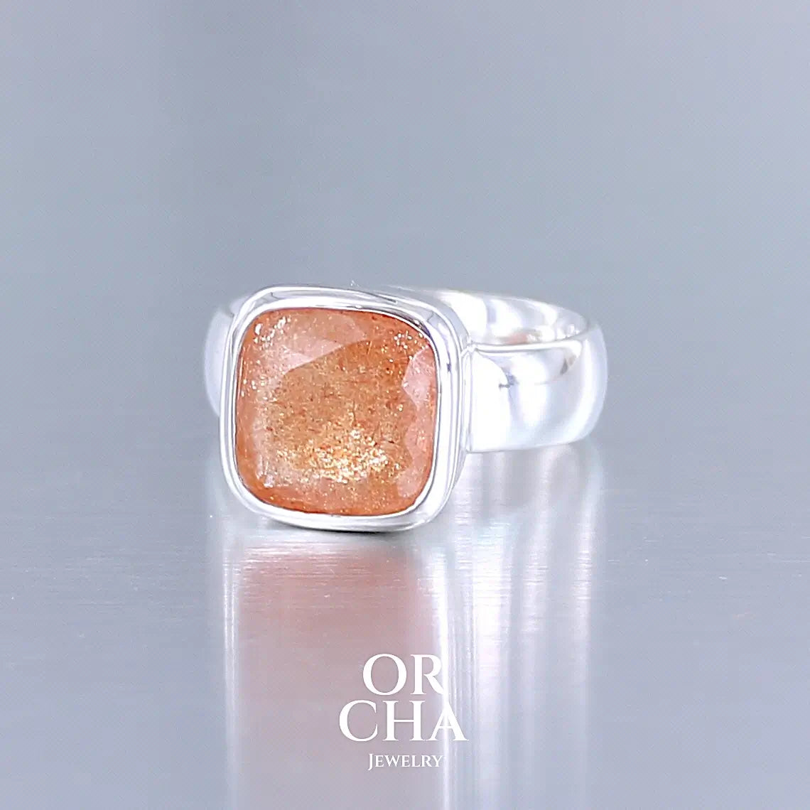 photo de profil d'une bague cocktail pour femme en argent massif sertie d'une pierre de soleil oranges de très belle qualité, pierre transparente avec inclusions scintillantes d'hématites. Pierre naturelle facettée de forme carrée. Tailles 56. Bijoux unique, éthique et durable présenté dans un coffret de notre marque, prêt à offrir. Livraison offerte, certificat d'authenticité, service client.