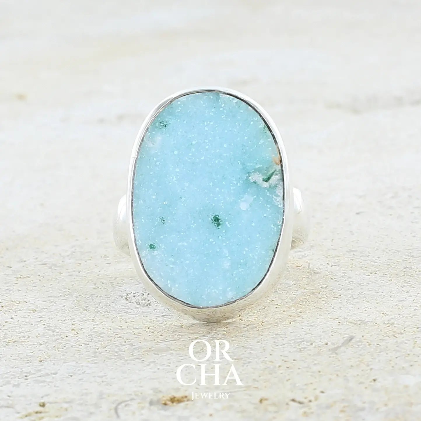 Bague pour femme en argent massif sertie d'un magnifique gemsilica druzy: chrysocale silicifiée recouverte de fins cristaux de quartz scintillants. Pierre de qualité opaque taillée en tranche de forme ovale. Pierre naturelle originaire de République dominicaine du Congo de couleur bleu clair turquoise. Bague réalisée en taille 58,5. Bijoux unique, éthique et durable présenté dans un coffret de notre marque, prêt à offrir. Livraison offerte, certificat d'authenticité, service client.