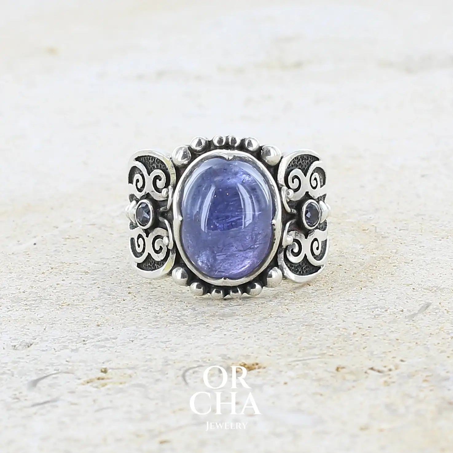 Bague en argent massif sculptées d'entrelacs de style celtique qui illustrent des papillons, sertie d'une Tanzanite. Pierre cabochon de forme ovale, de couleur bleu lavande foncé, de qualité transparente avec inclusions. Taille 56. Bijoux unique, éthique et durable présenté dans un coffret de notre marque, prêt à offrir. Livraison offerte, certificat d'authenticité, service client.