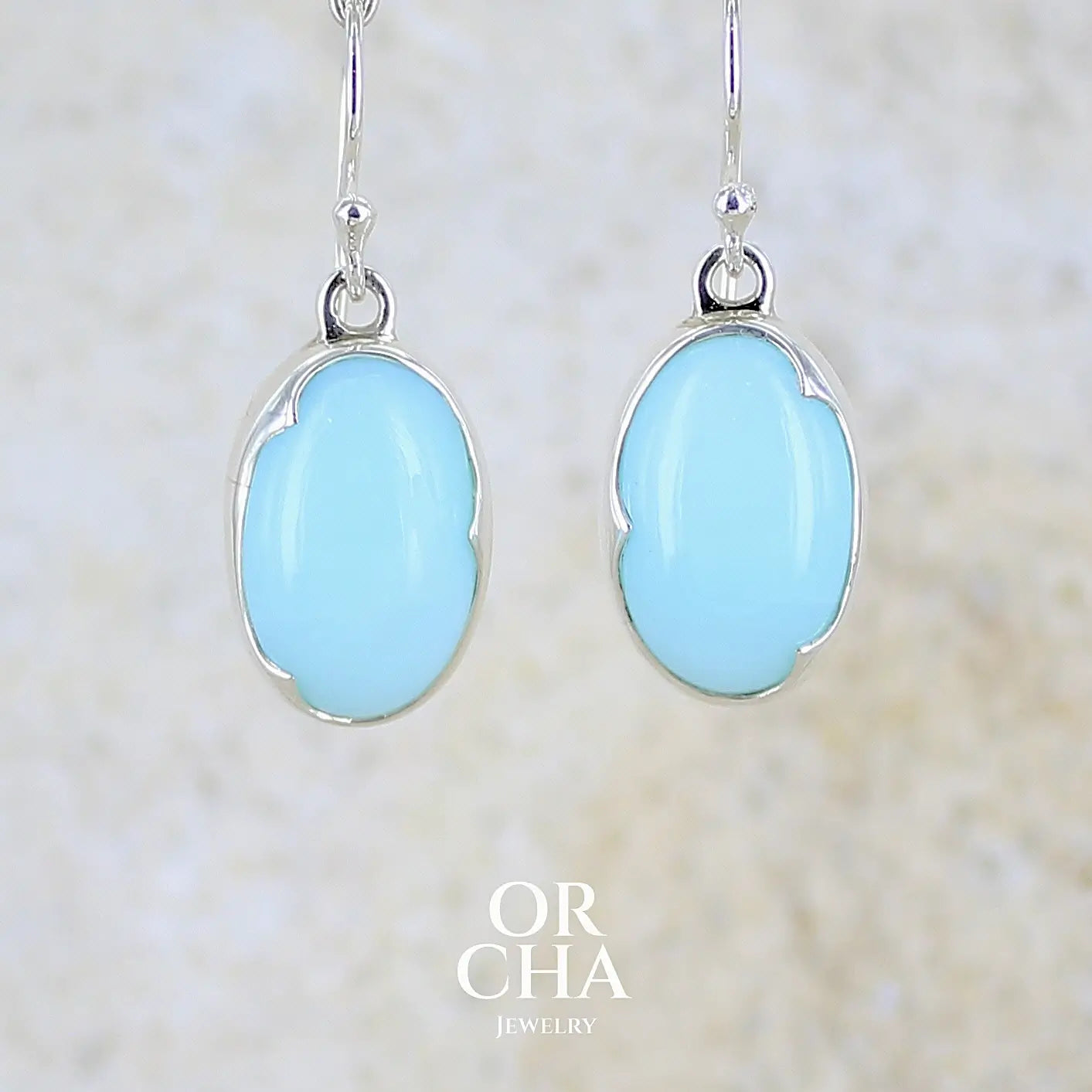 Boucles d'oreilles pendantes en argent massif serties d'opale bleue du Pérou. Pierres cabochon taillée en ovale de qualité opaque. Pierre naturelle de couleur bleu ciel. Bijoux unique, éthique et durable présenté dans un coffret de notre marque, prêt à offrir. Livraison offerte, certificat d'authenticité, service client.