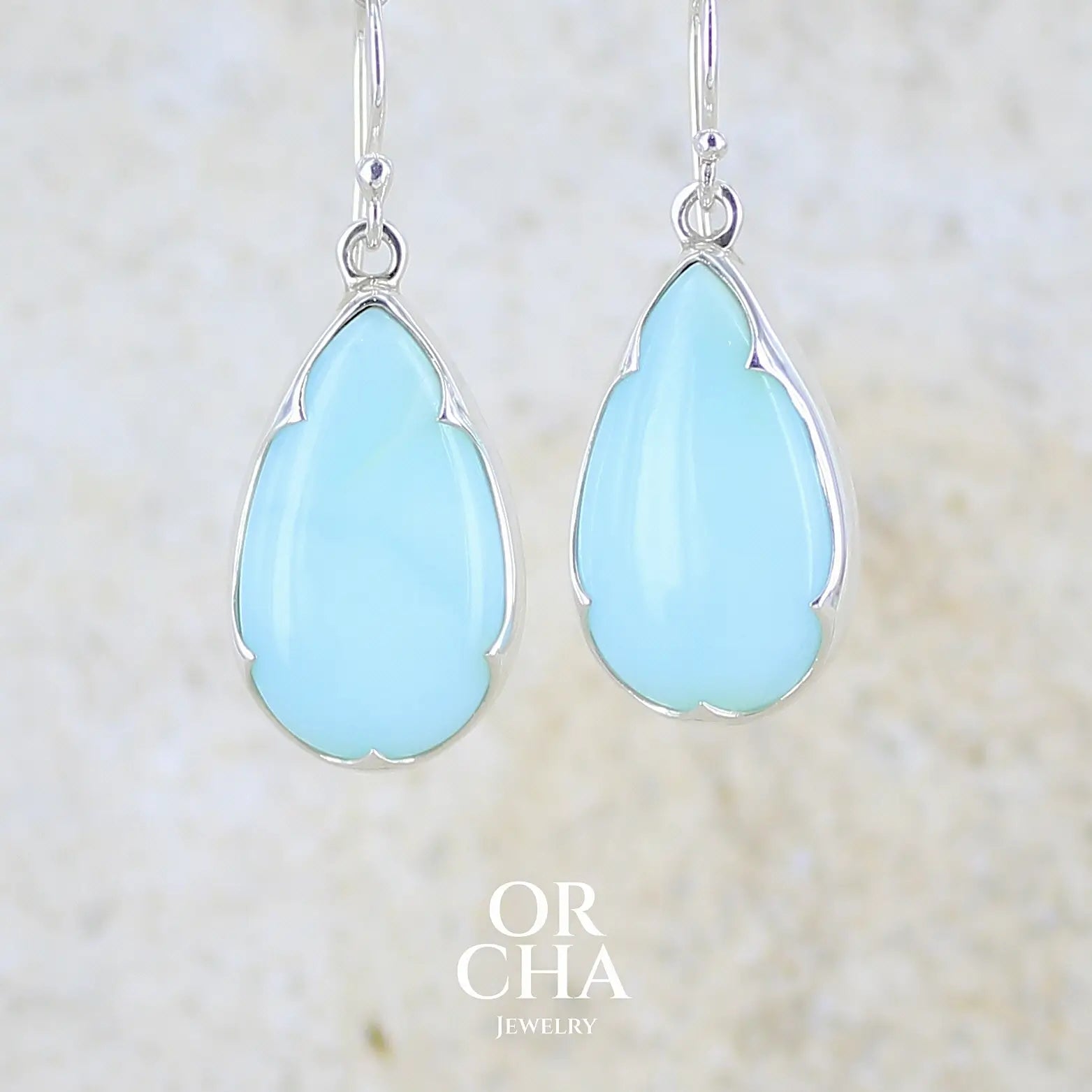 Boucles d'oreilles pendantes en argent massif serties d'opale bleue du Pérou. Pierres cabochon taillée en goutte de qualité opaque. Pierre naturelle de couleur bleu ciel. Bijoux unique, éthique et durable présenté dans un coffret de notre marque, prêt à offrir. Livraison offerte, certificat d'authenticité, service client.