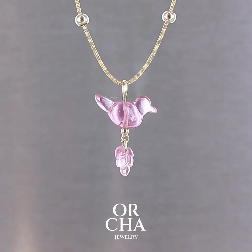 Collier pour femme orné d'une tourmaline rose sculptée à la main en 3 dimensions en forme d'oiseau et de feuille, serties en or 18k. Le pendentif est monté sur un collier corde doré scintillant, les apprêts utilisé sont en Gold filled ( or laminé ). Longueur ajustable de 40 cm à 45 cm. Bijoux unique, éthique et durable présenté dans un coffret de notre marque, prêt à offrir. Livraison offerte, certificat d'authenticité, service client.