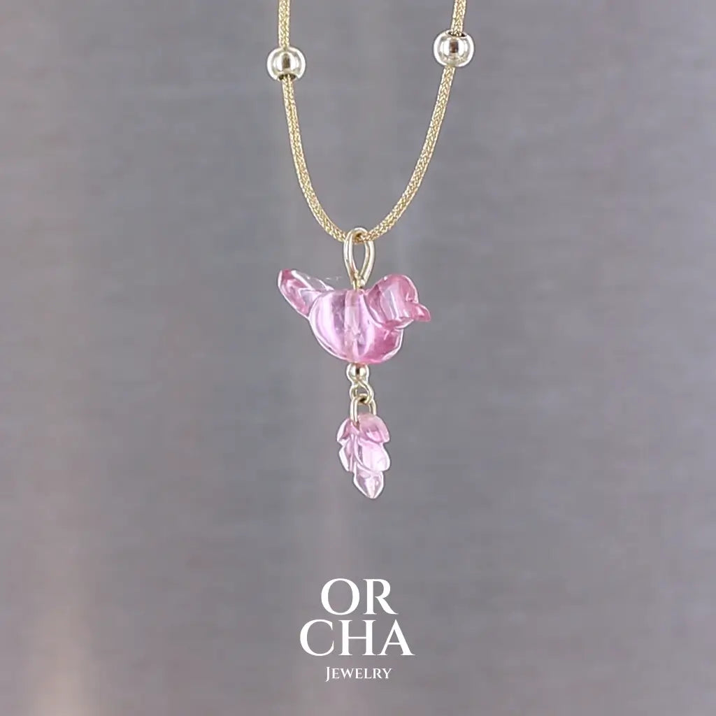 Collier pour femme orné d'une tourmaline rose sculptée à la main en 3 dimensions en forme d'oiseau et de feuille, serties en or 18k. Le pendentif est monté sur un collier corde doré scintillant, les apprêts utilisé sont en Gold filled ( or laminé ). Longueur ajustable de 40 cm à 45 cm. Bijoux unique, éthique et durable présenté dans un coffret de notre marque, prêt à offrir. Livraison offerte, certificat d'authenticité, service client.