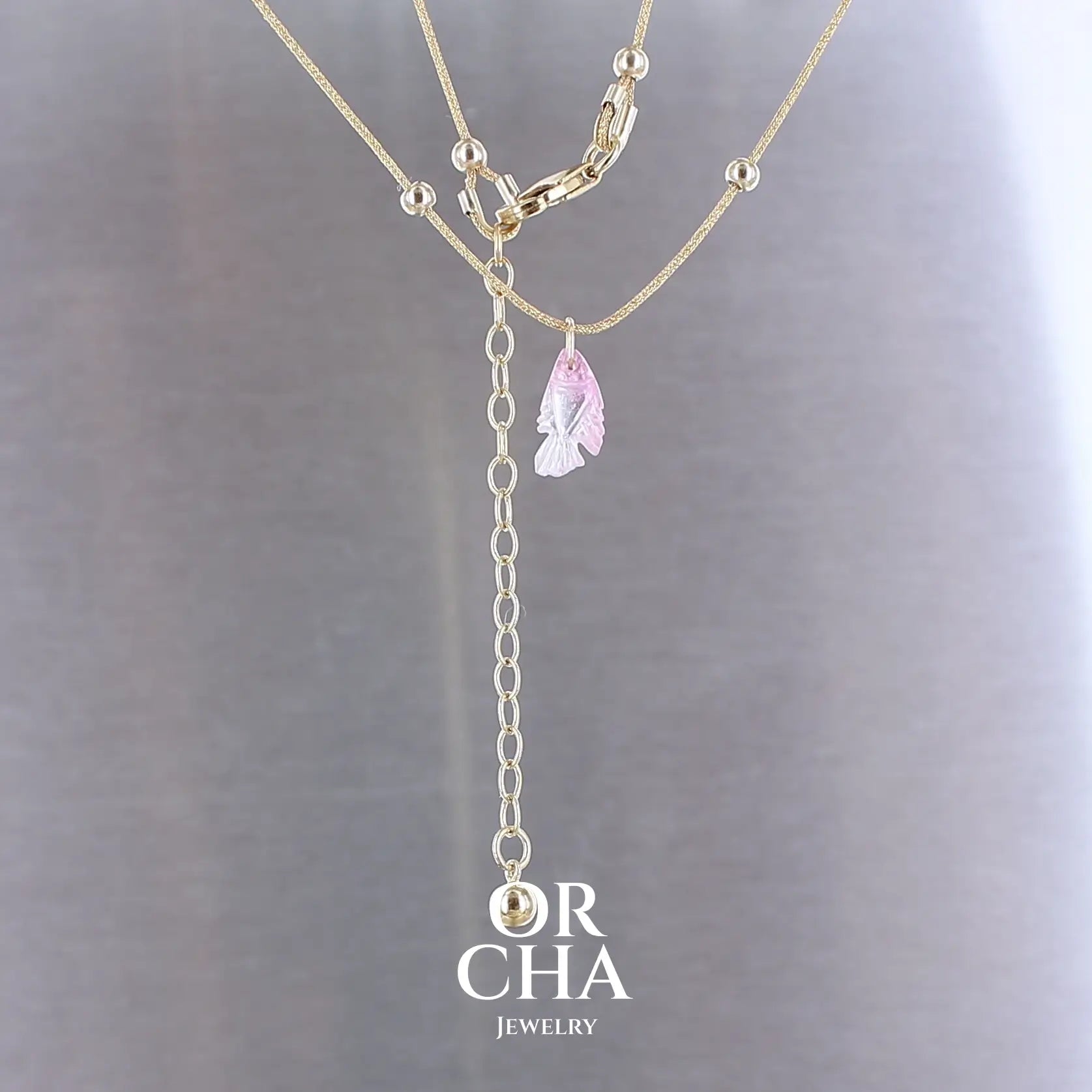 Collier pour femme orné d'une tourmaline rose sculptée à la main en 3 dimensions en forme de poisson sertie en or 18k. Le pendentif est monté sur un collier corde doré scintillant, les apprêts utilisé sont en Gold filled ( or laminé ). Longueur ajustable de 40 cm à 45 cm. Bijoux unique, éthique et durable présenté dans un coffret de notre marque, prêt à offrir. Livraison offerte, certificat d'authenticité, service client.