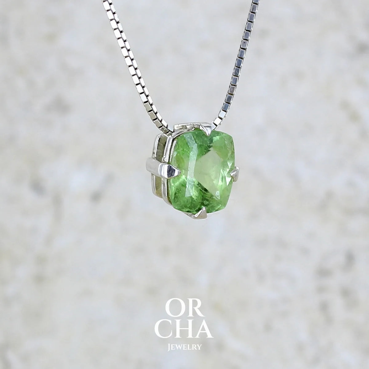 détail collier solitaire pour femme en argent massif sertie d'un Péridot de couleur vert pastel anisé. Pierre facettée de forme carrée, qualité transparente présentant des inclusions. Pendentif monté sur une chaine en argent sterling de type maille miroir de 1,3 mm d'épaisseur et de 40cm de longueur. Bijoux unique réalisé par Orchajewelry