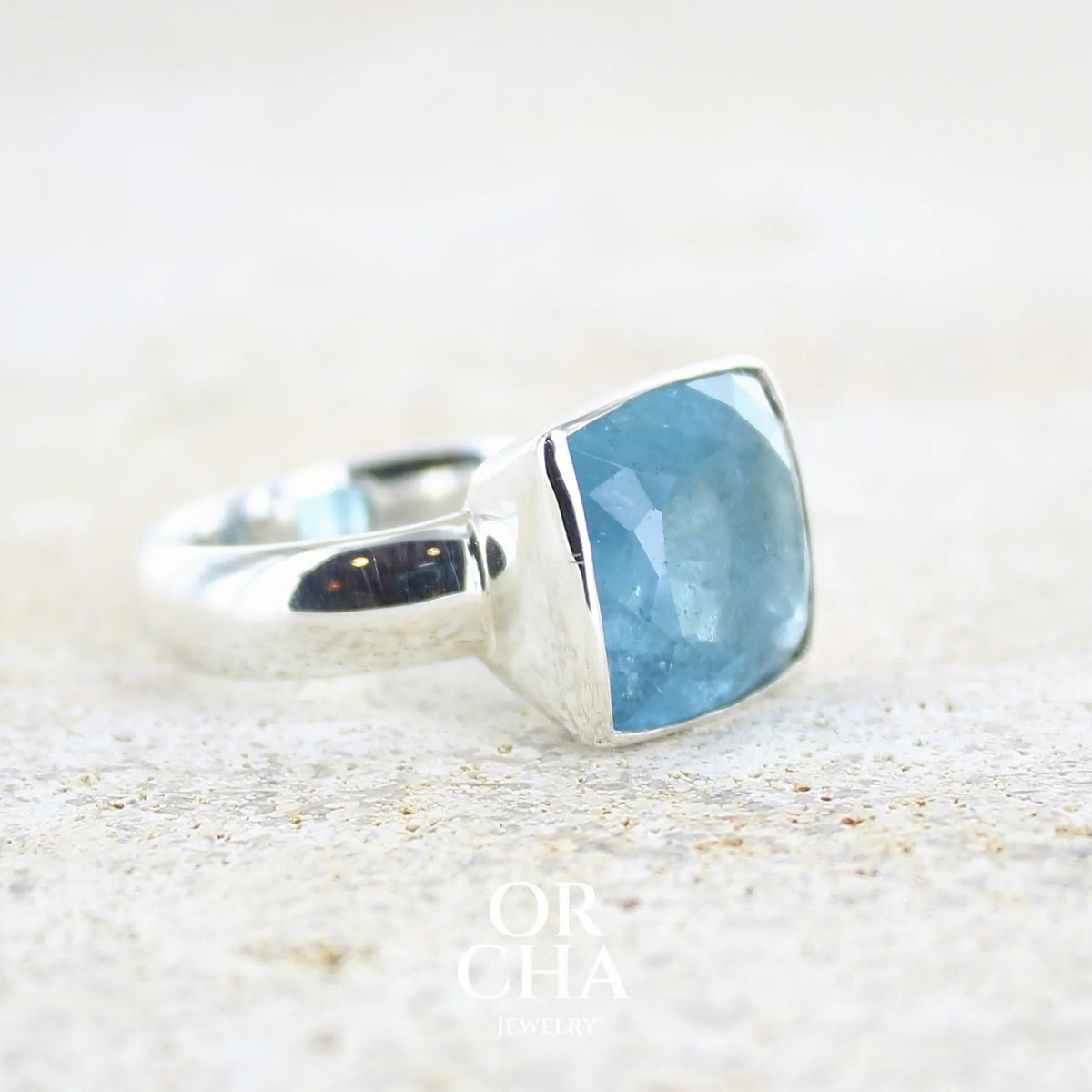 detail du sertissage d'une Bague cocktail pour femme en argent massif sertie d'une aigue marine taillée de 10 carats de couleur bleue gris foncé, pierre transparente avec inclusions. Pierre naturelle facettée de forme rectangulaire. Bijoux unique réalisée en taille 60,5 par Orchajewelry